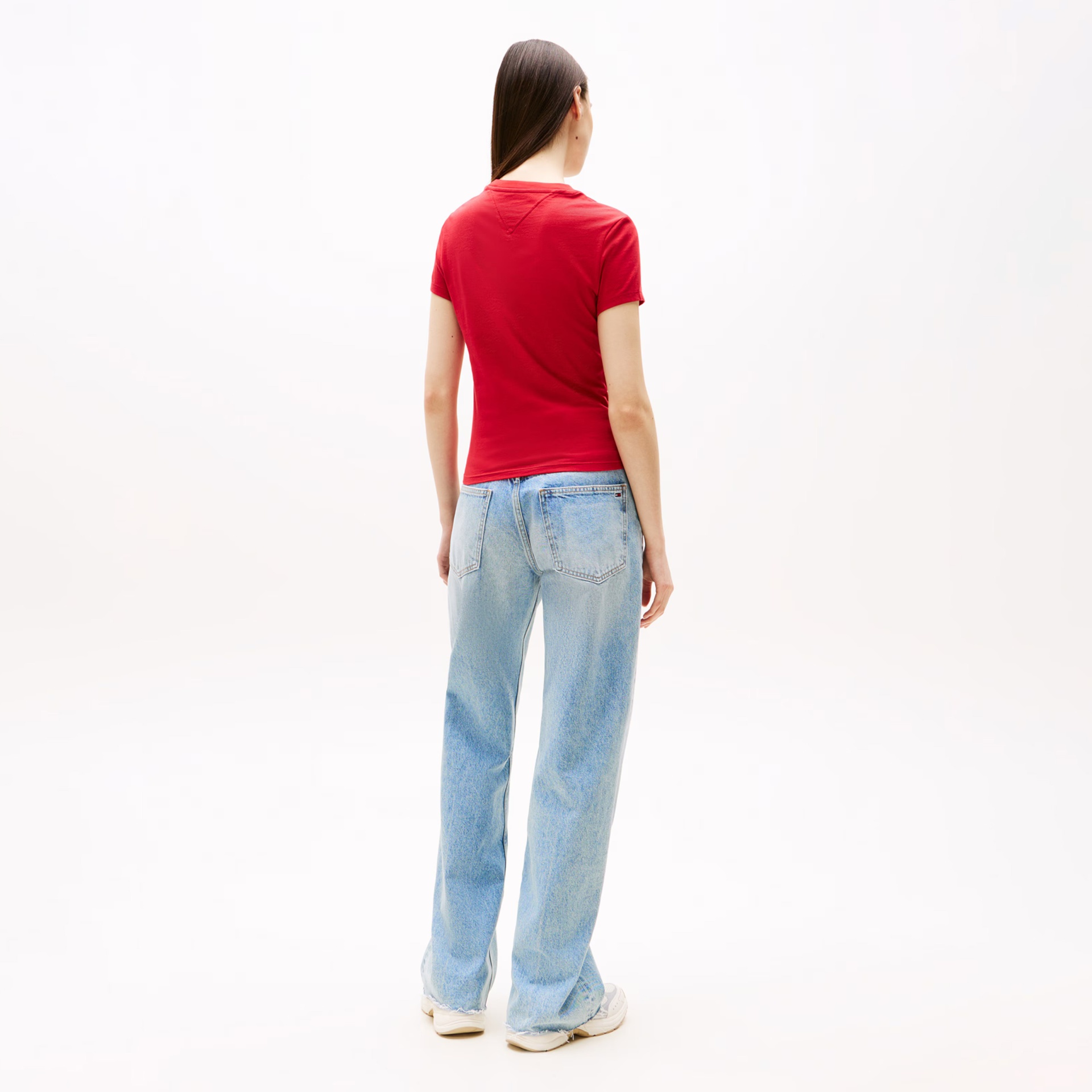 Mulher vista de costas a vestir calças de ganga azuis claras, t-shirt vermelha e sapatilhas brancas