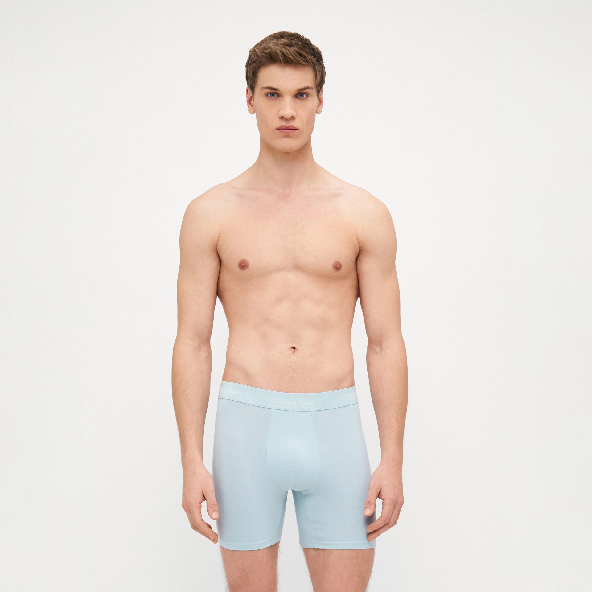Homem a usar cuecas boxer azuis claras Calvin Klein com fundo branco.
