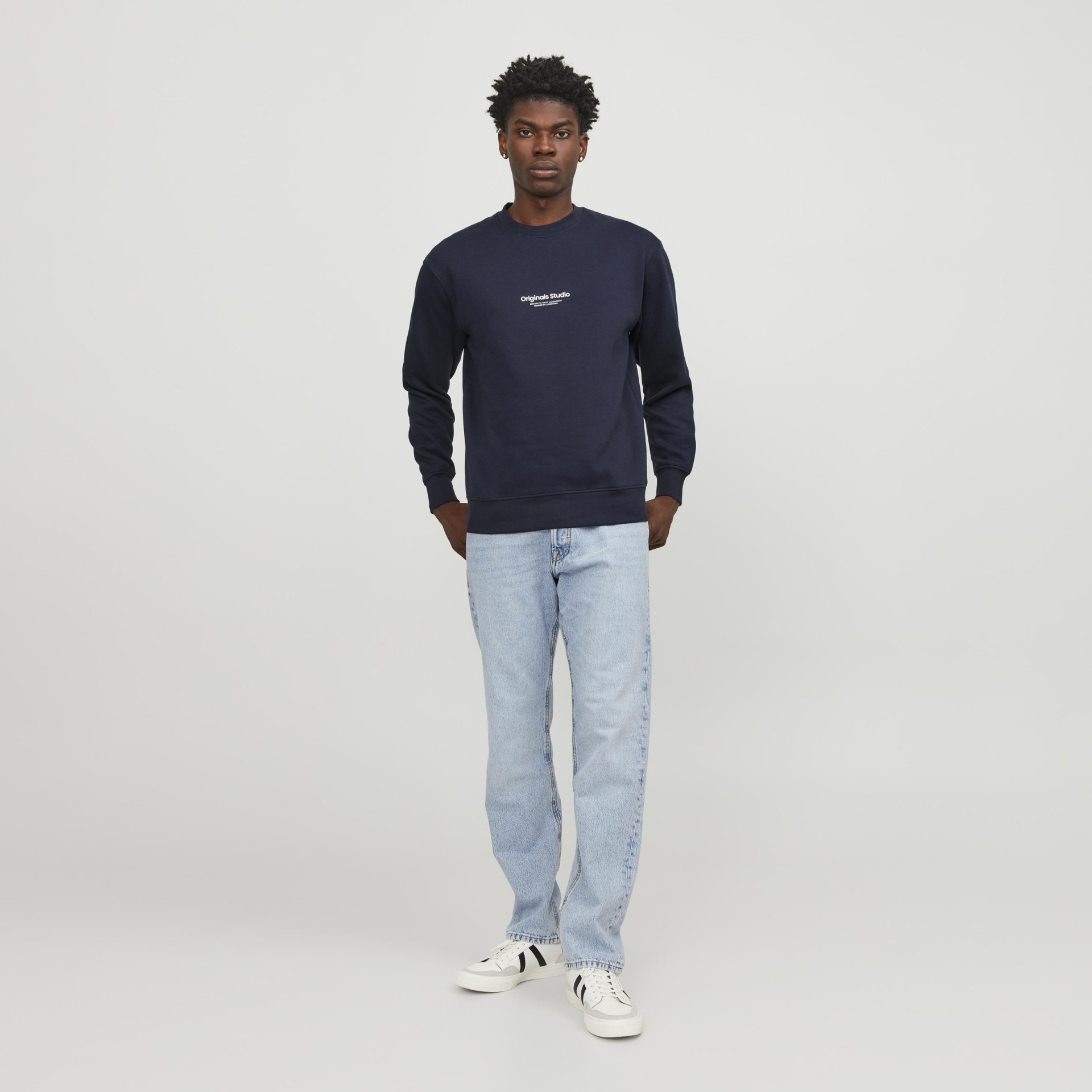 Homem com sweat azul escuro Originals Studio, jeans azul claro e ténis brancos