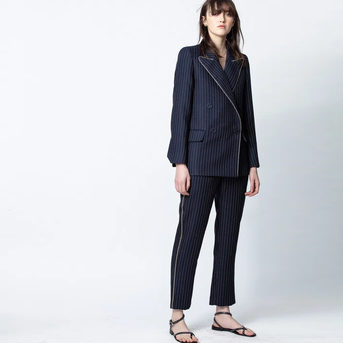 Fato feminino azul escuro risca de giz com blazer e calças combinadas, sapatos pretos, fundo branco.