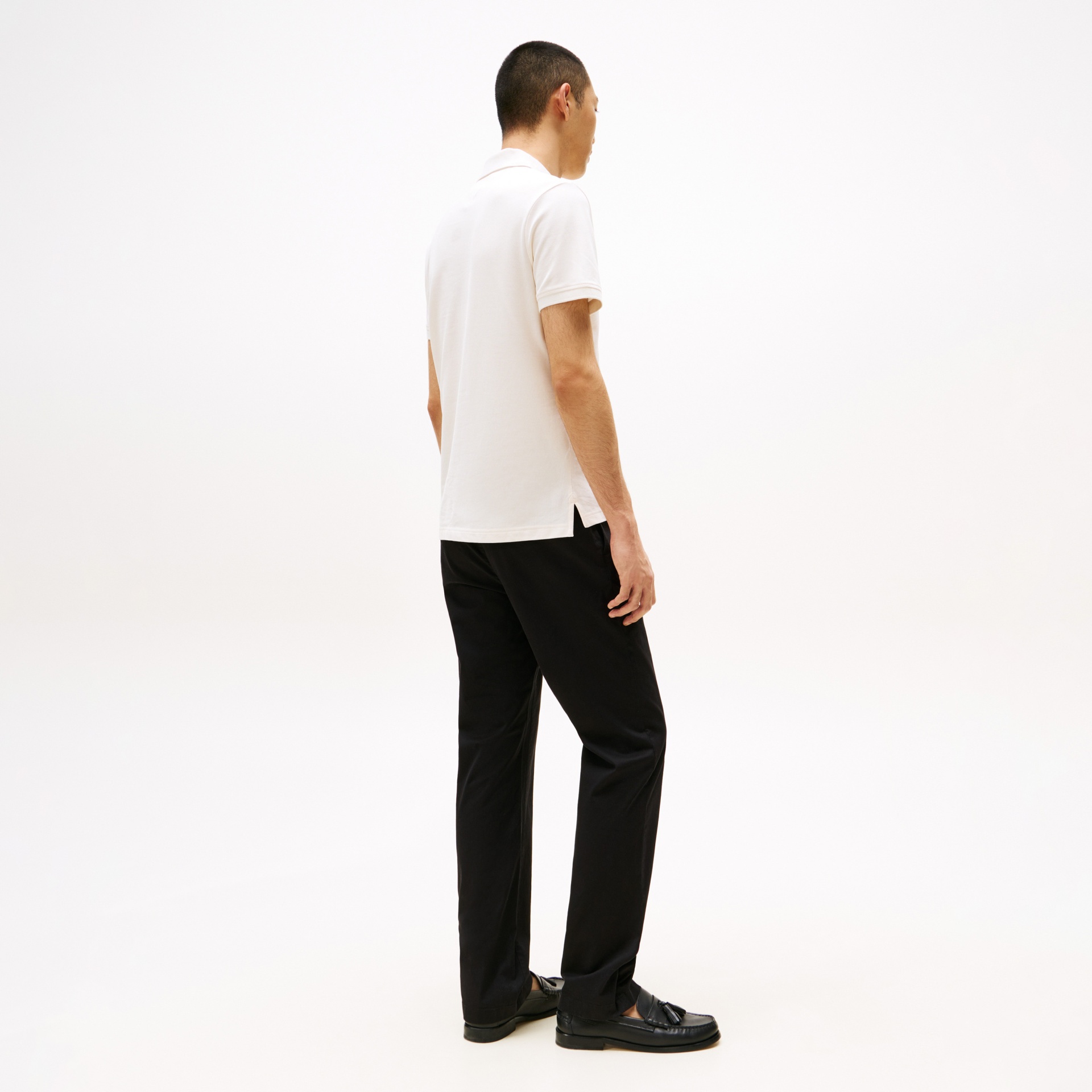 Homem com polo branca e calças pretas visto de costas