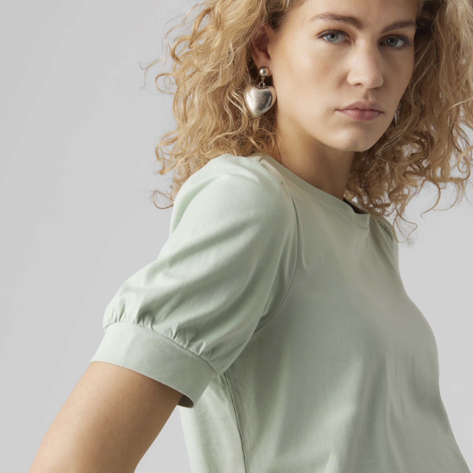 Camiseta verde clara de mangas curtas com punhos e mulher loira com brincos grandes de coração