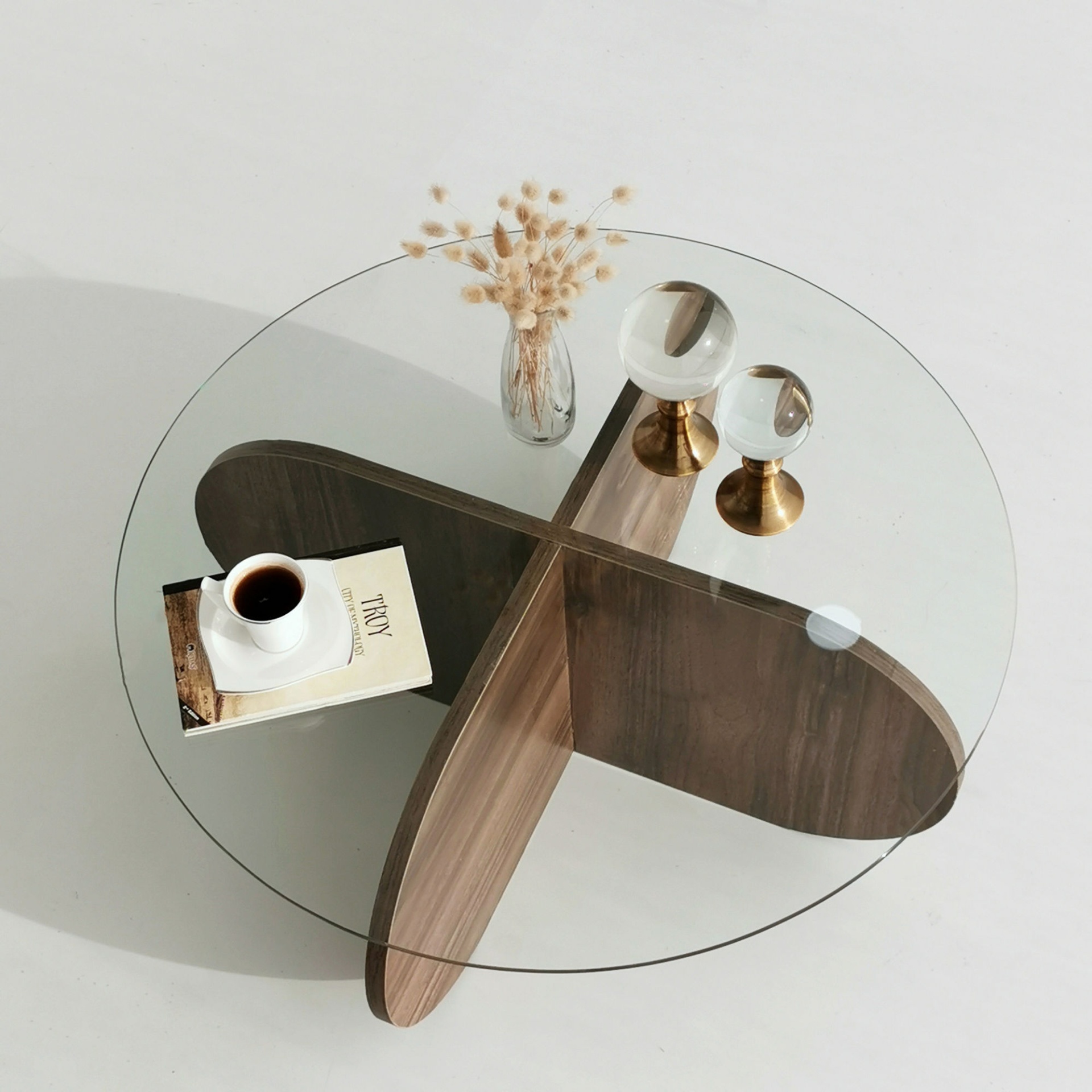 Mesa de centro redonda de vidro e madeira com café, livro, vaso de flores e suportes de bolas de vidro
