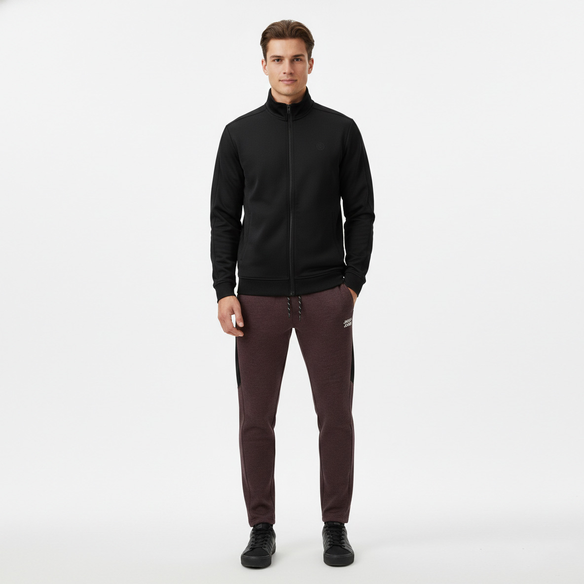 Homem com casaco desportivo preto, calças de treino bordô com texto JACK & JONES e ténis pretos