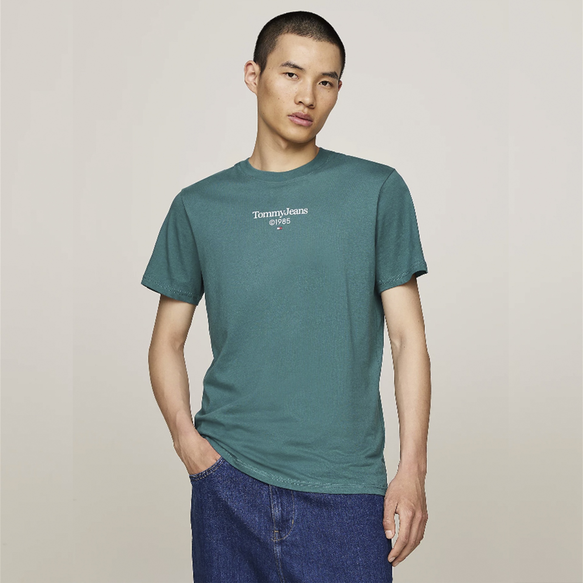 Camiseta verde-azulada com texto Tommy Jeans EST.85 e calças jeans azuis