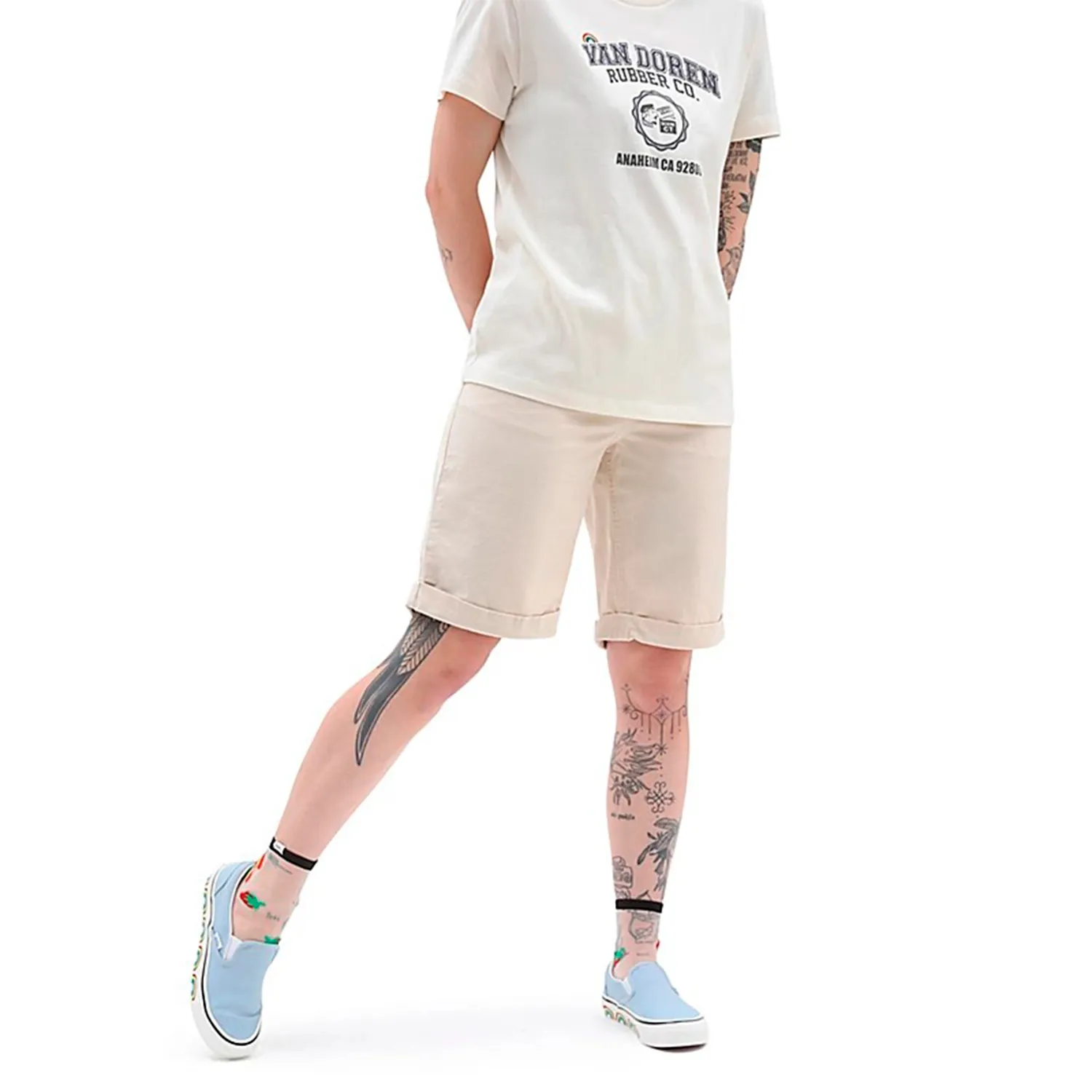 Pessoa com t-shirt branca com texto, calções bege e sapatilhas azuis com sola branca