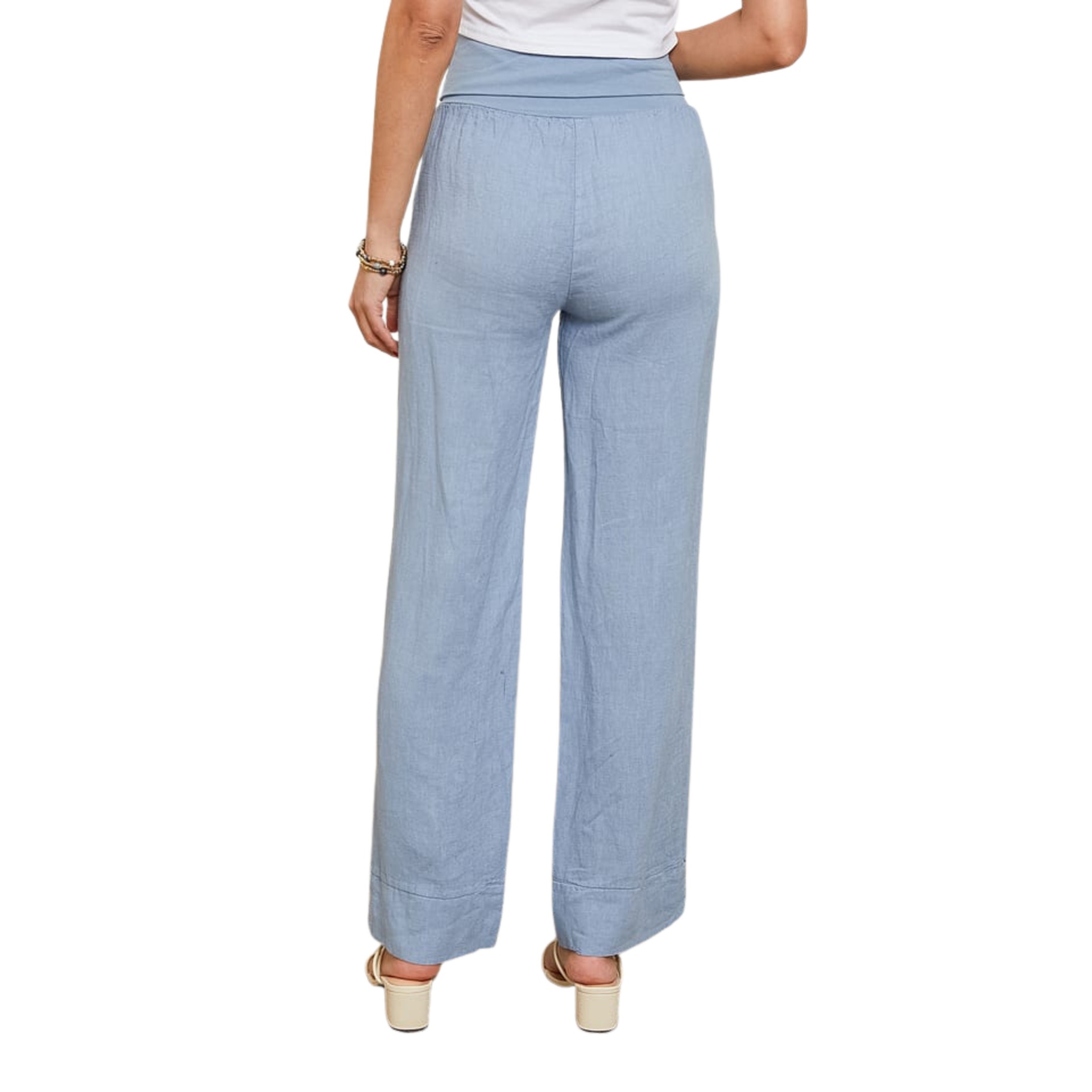 Calças femininas azuis compridas vistas de costas com sandálias creme