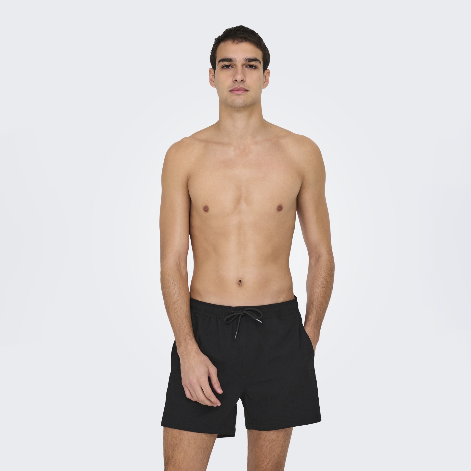 Homem sem camisa com calções pretos e cordão na cintura, sobre fundo branco