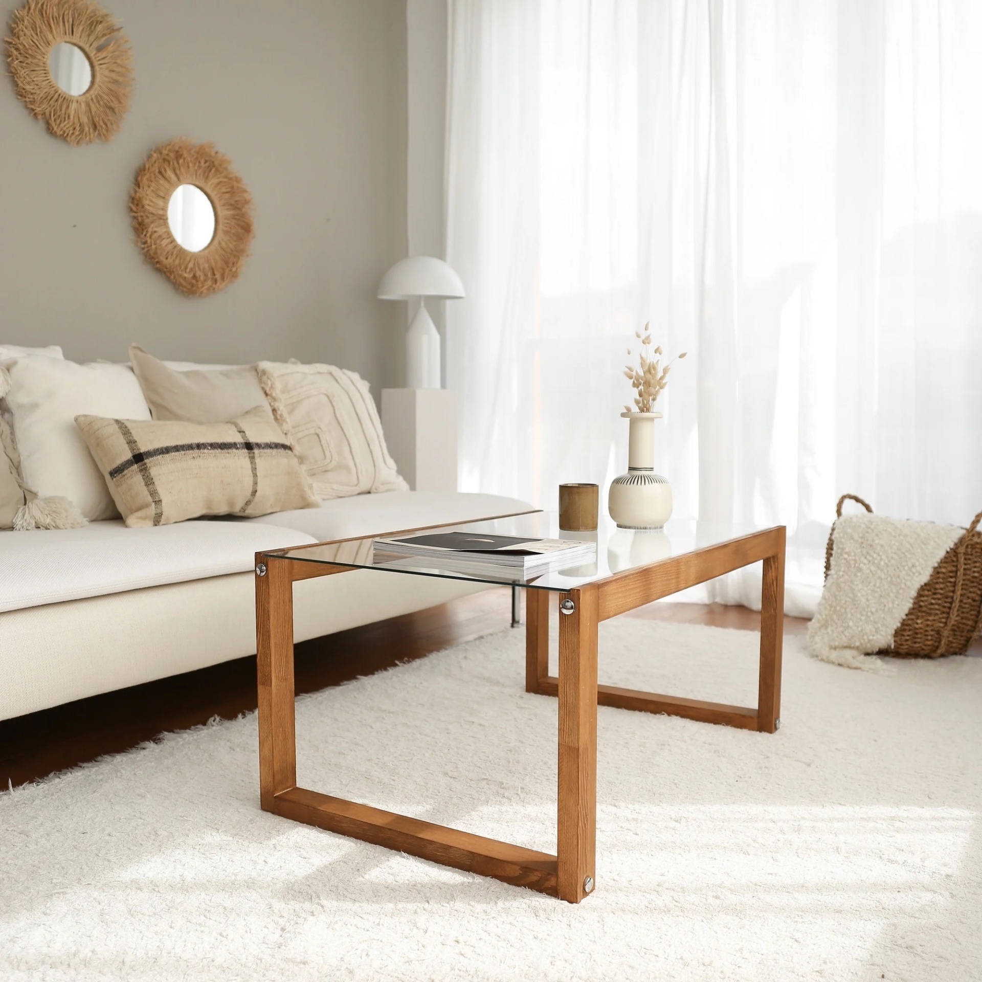 Mesa de centro de vidro e madeira numa sala clara com sofá e decoração neutra