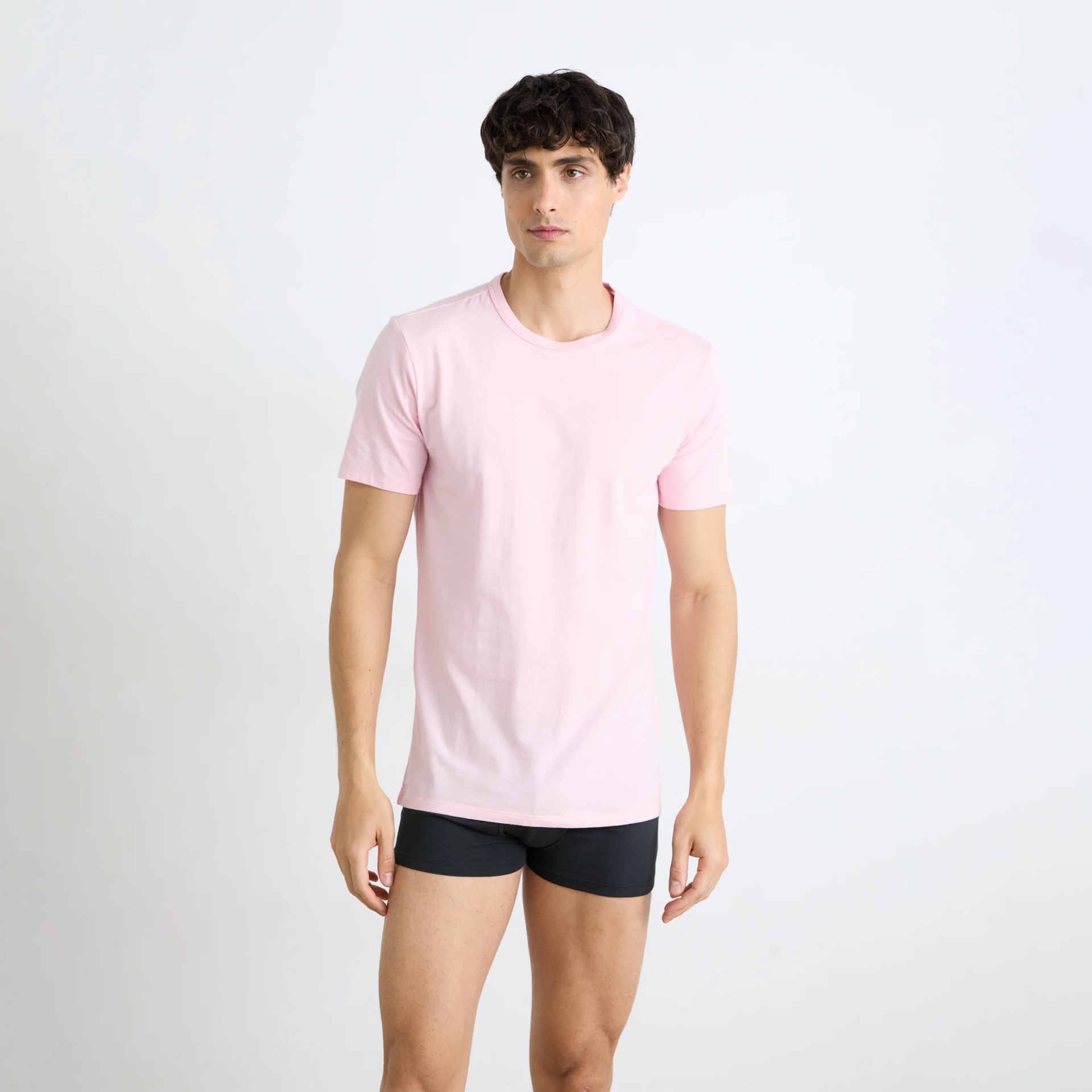 Homem a usar t-shirt cor-de-rosa e cuecas pretas, em fundo branco.