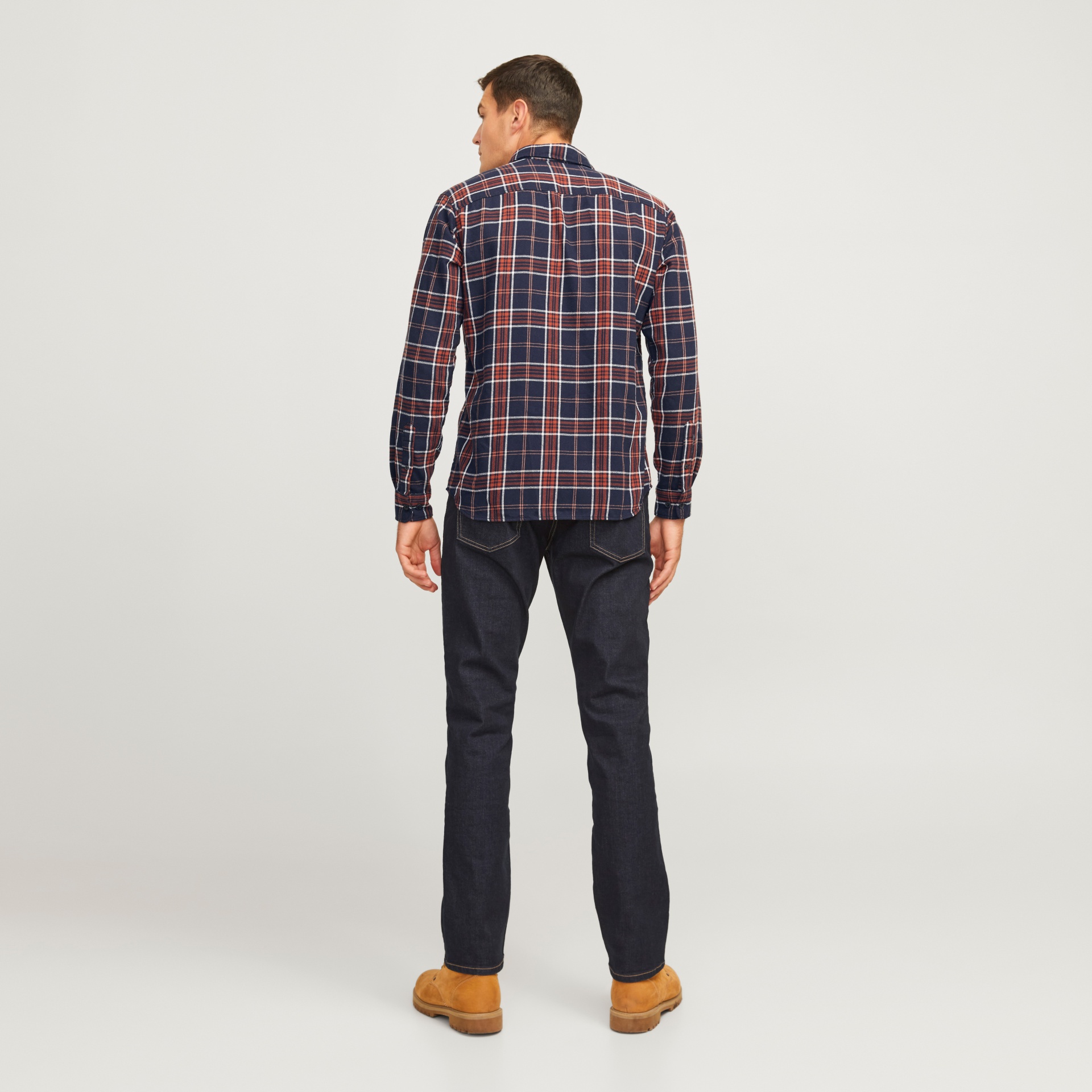 Homem de costas com camisa xadrez, jeans escuro e botas castanhas