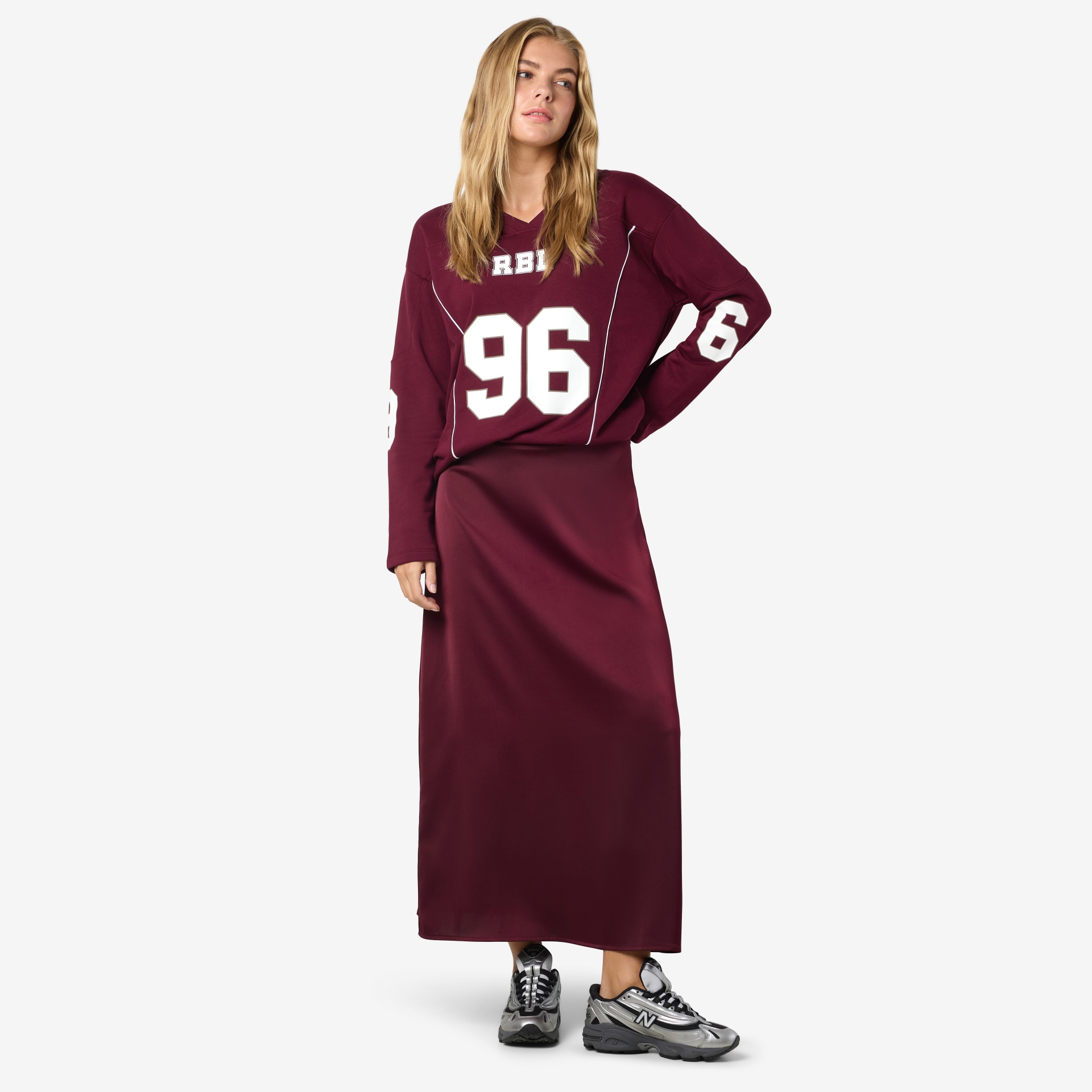 Mulher com sweatshirt grená estampada com números brancos e saia comprida da mesma cor, e ténis prata e preto.