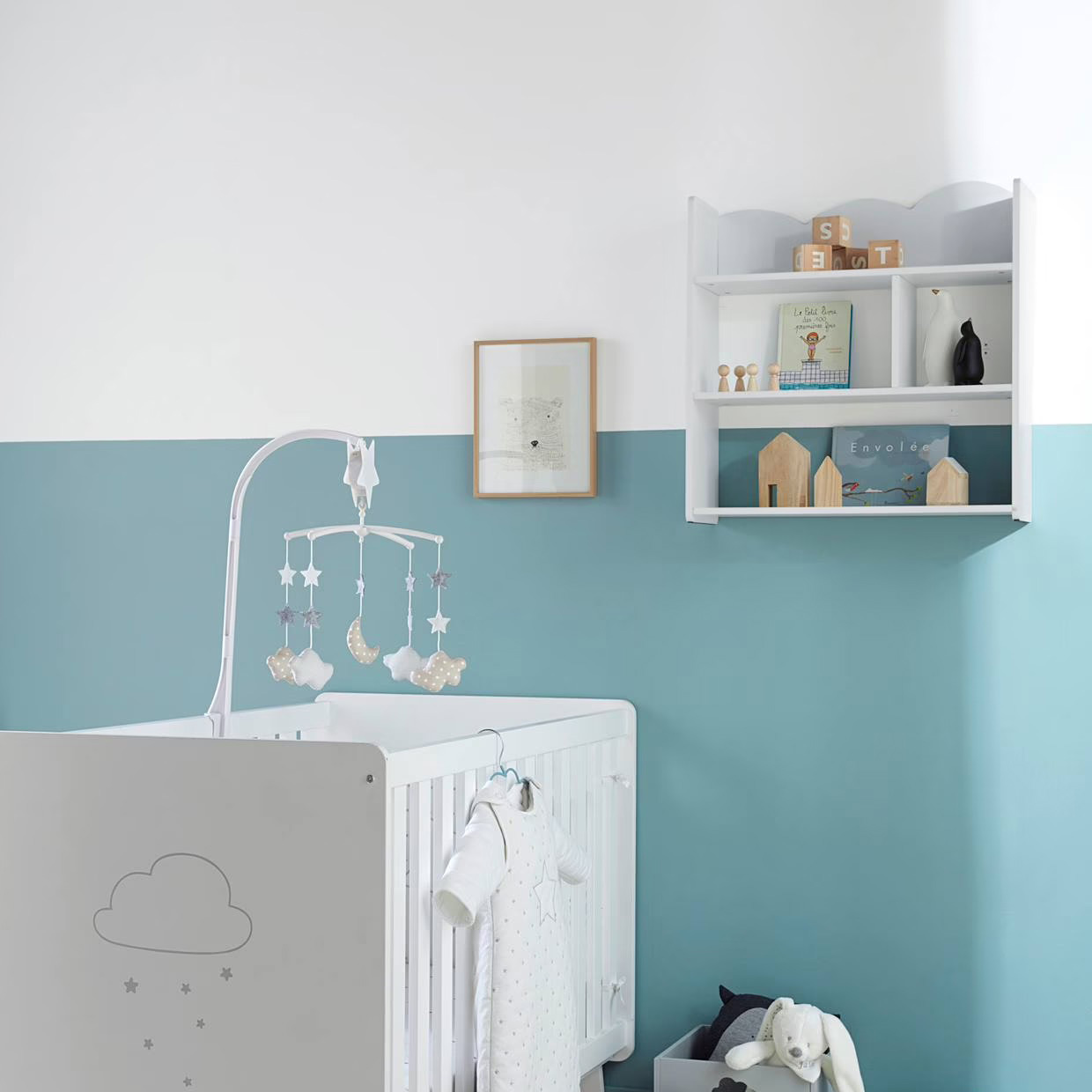 Quarto de bebé com berço branco, mó com estrelas e nuvens, prateleira branca, livros e decoração em madeira, parede azul e branca