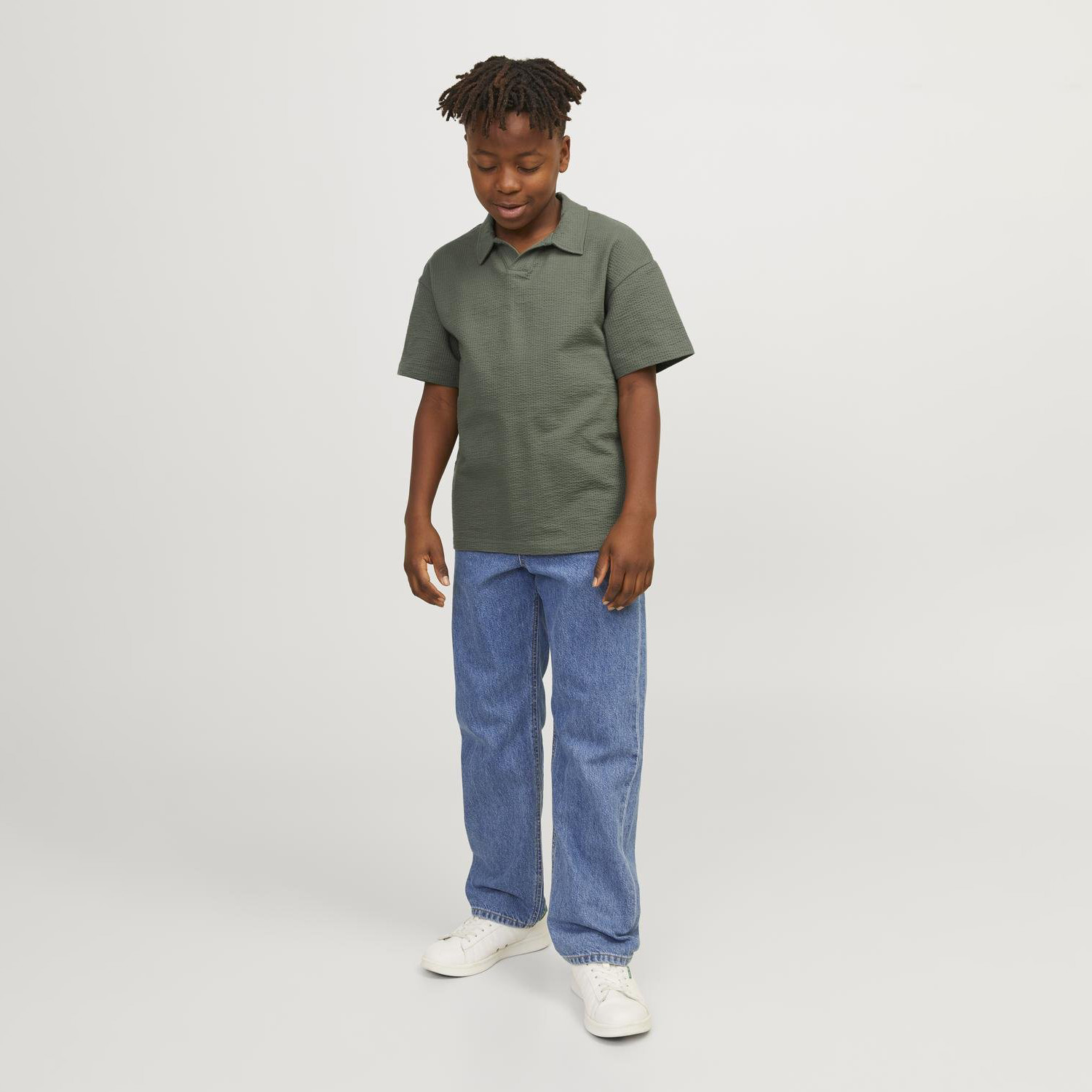 Rapaz com polo verde escuro e calças de ganga azuis com ténis brancos