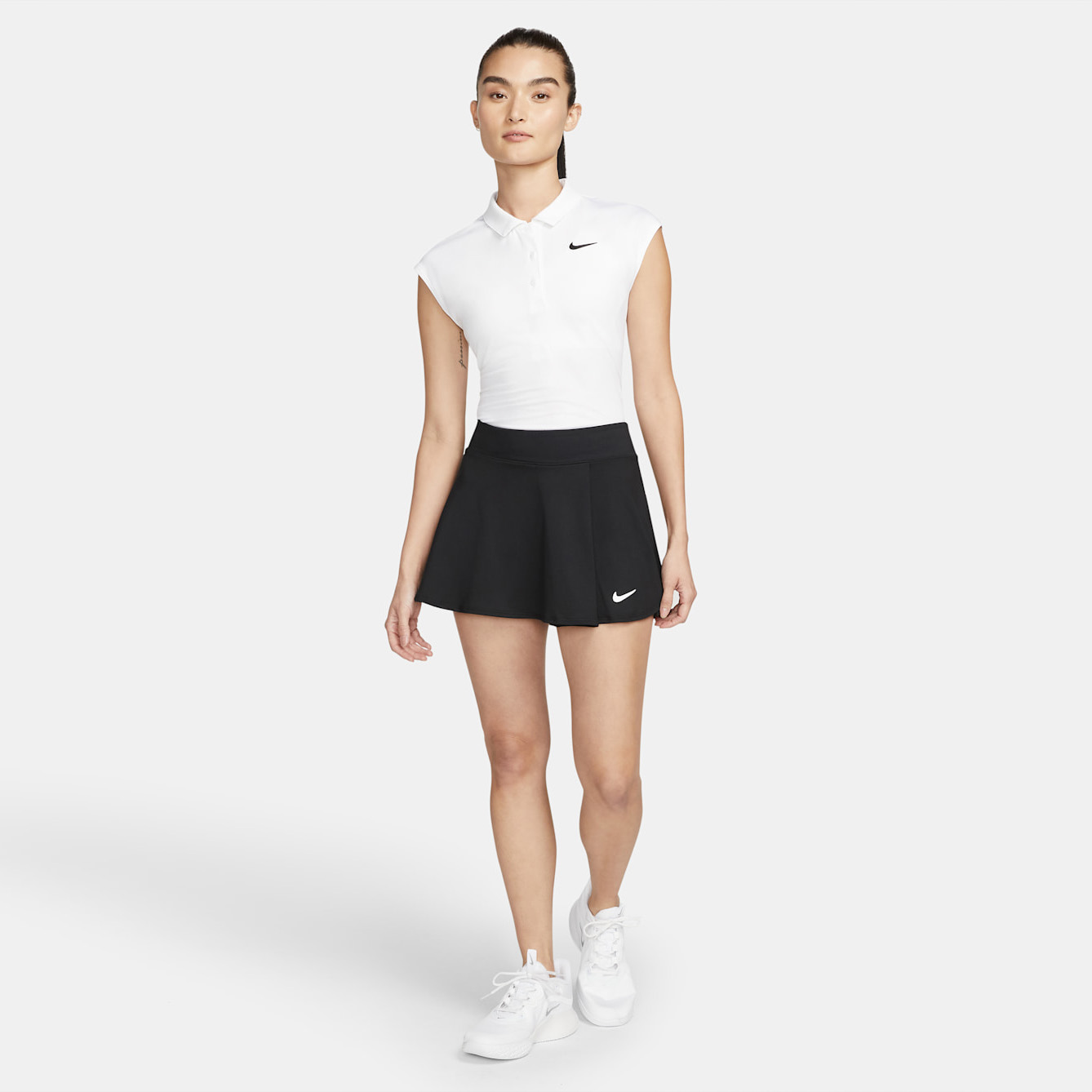 Mulher a vestir camisa polo branca, saia preta e ténis brancos com logos Nike