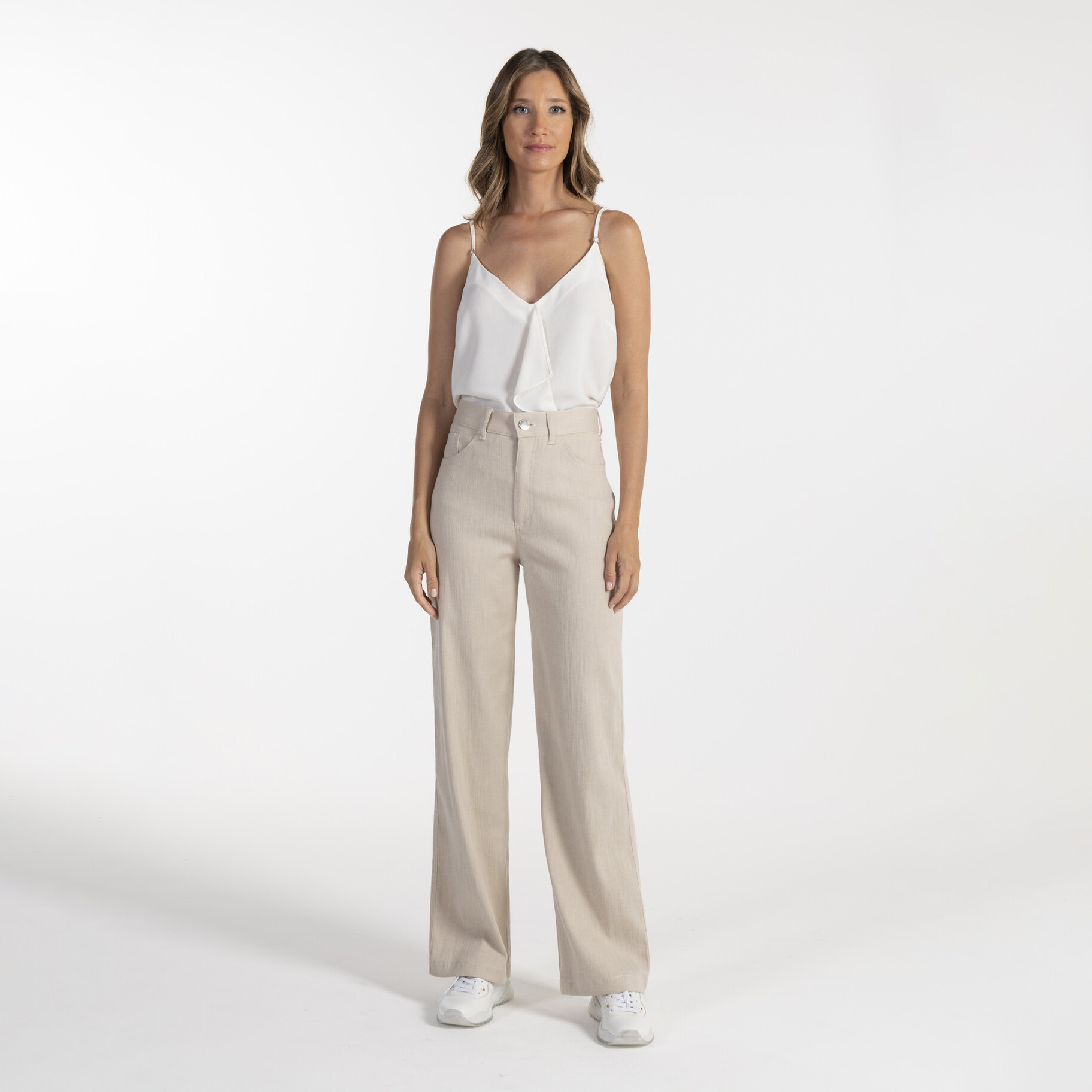 Mulher com top branco e calças beges em fundo branco