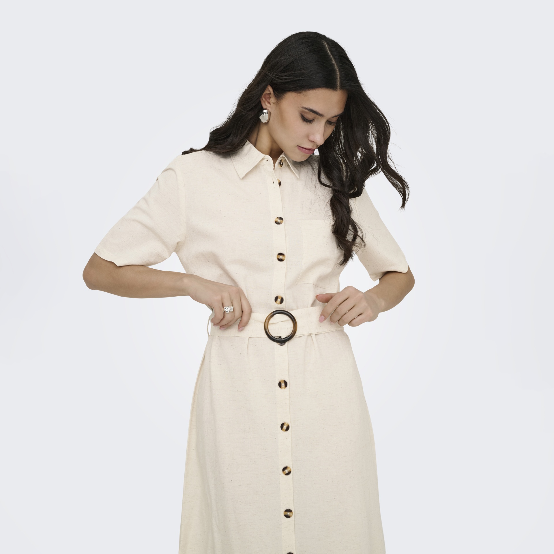 Vestido creme de manga curta com botões e cinto numa mulher de cabelo castanho escuro.