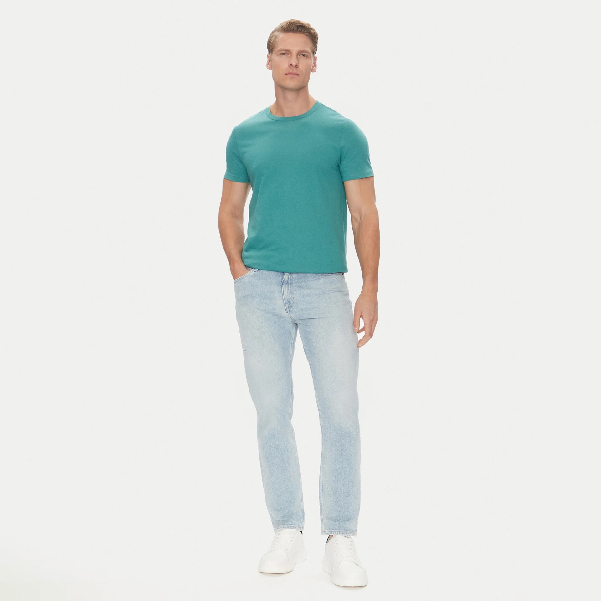 Homem com t-shirt azul-turquesa, jeans azuis claros e sapatilhas brancas