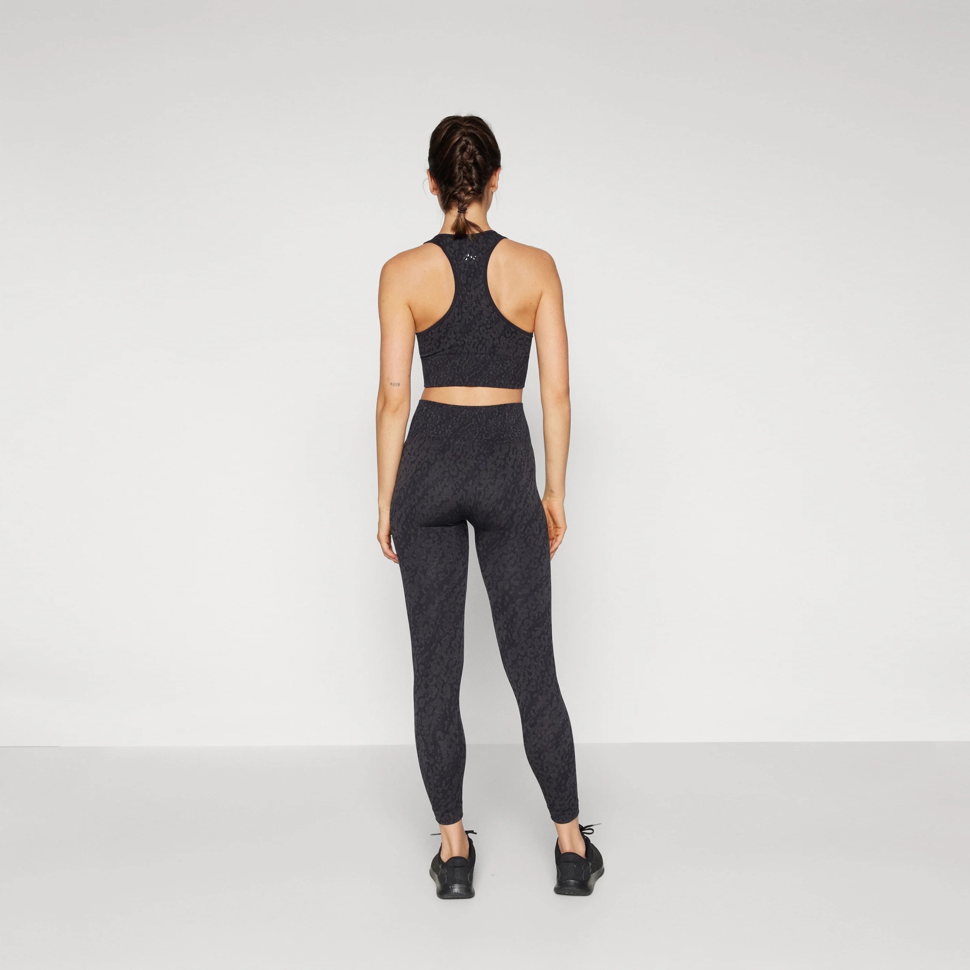 Conjunto desportivo cinza escuro com top e leggings em modelo feminino visto de costas