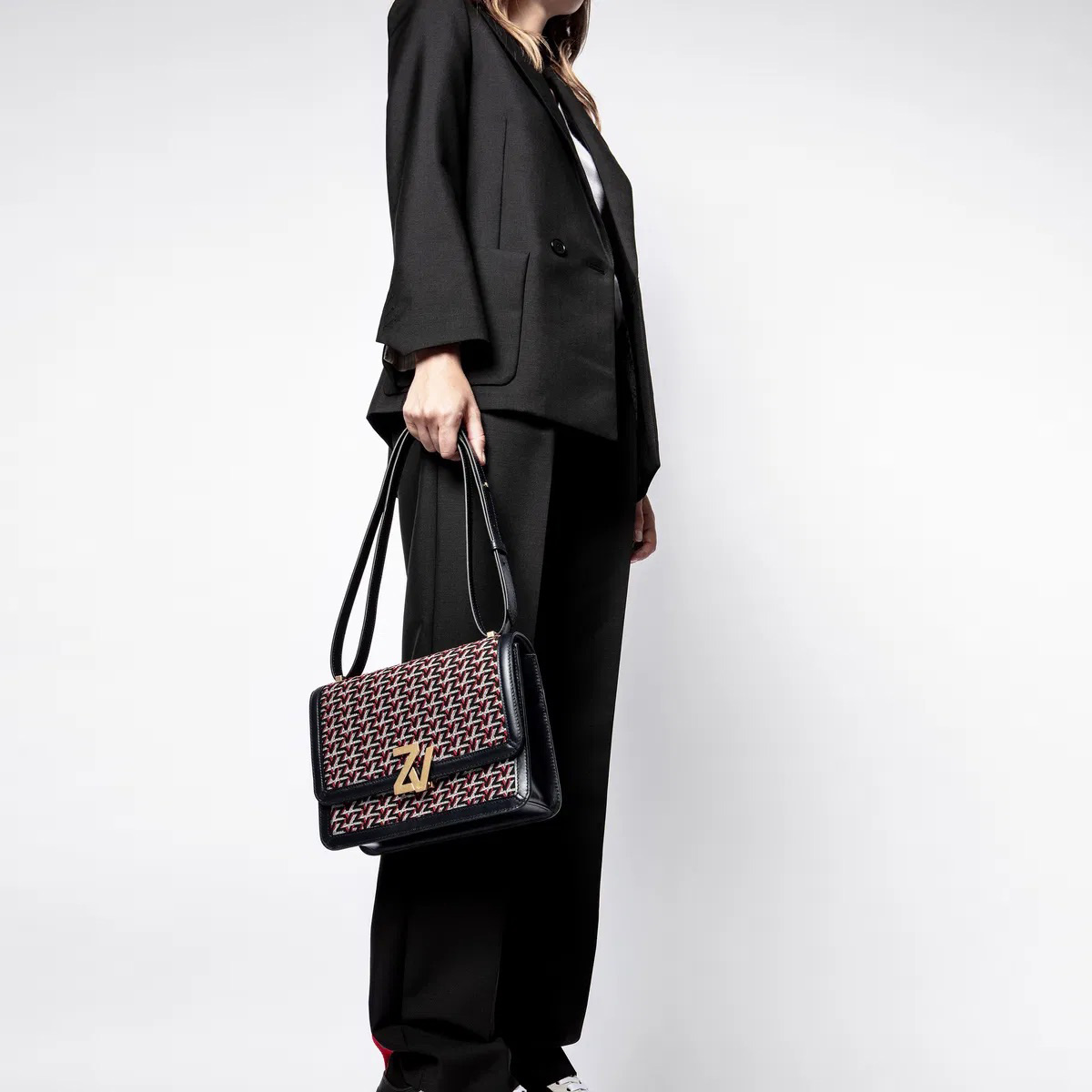 Mala carteira com padrão geométrico e detalhes dourados, segurada por pessoa vestida de preto