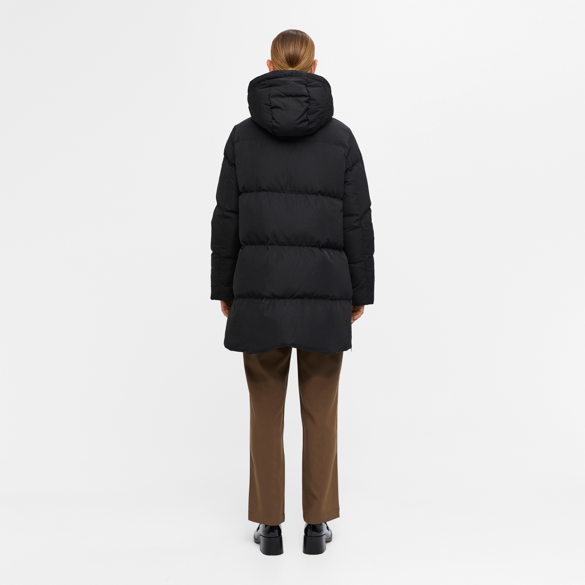 Casaco acolchoado preto com capuz visto de costas, pessoa com calças castanhas e sapatos pretos