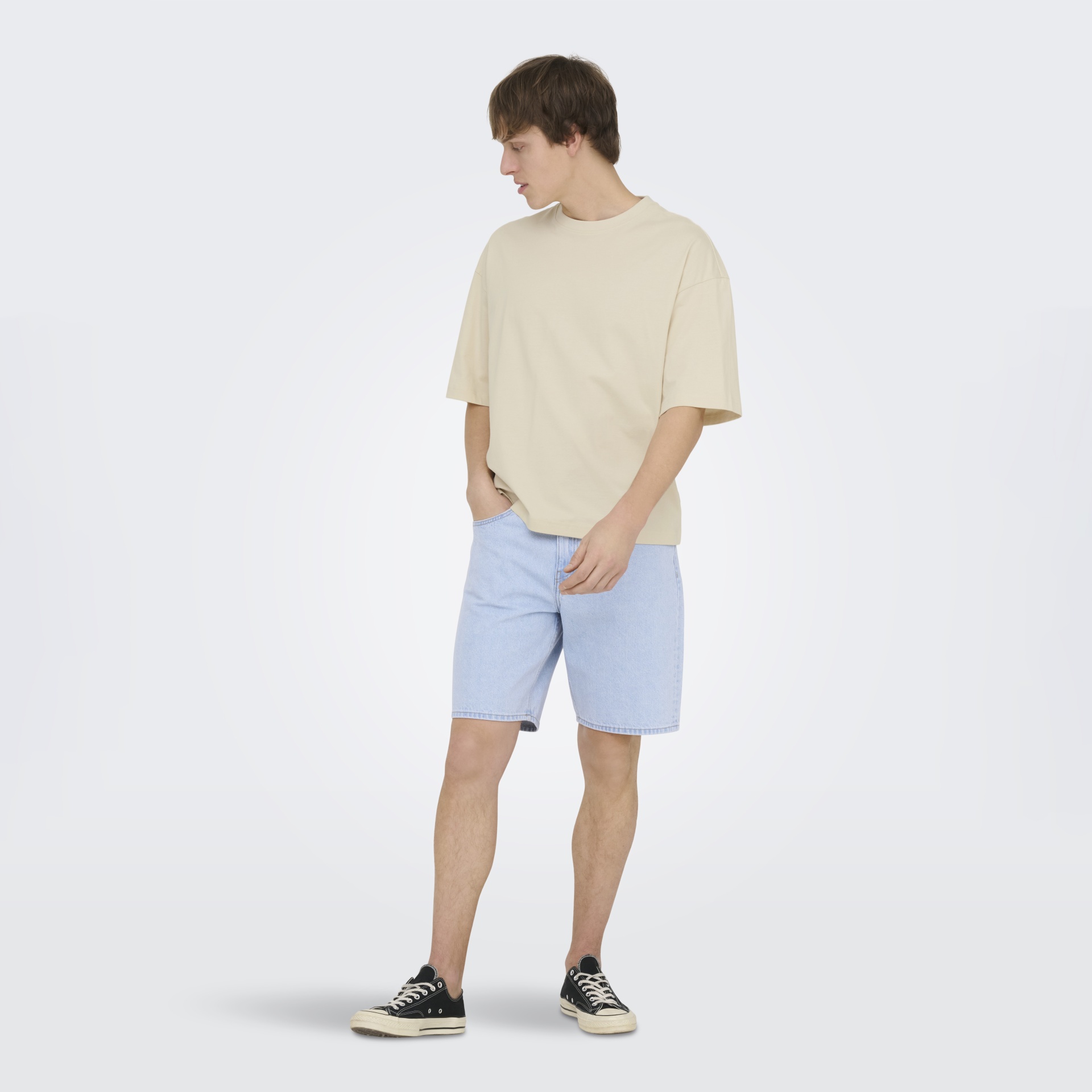 Homem com t-shirt bege, calções de ganga azuis claros e ténis pretos