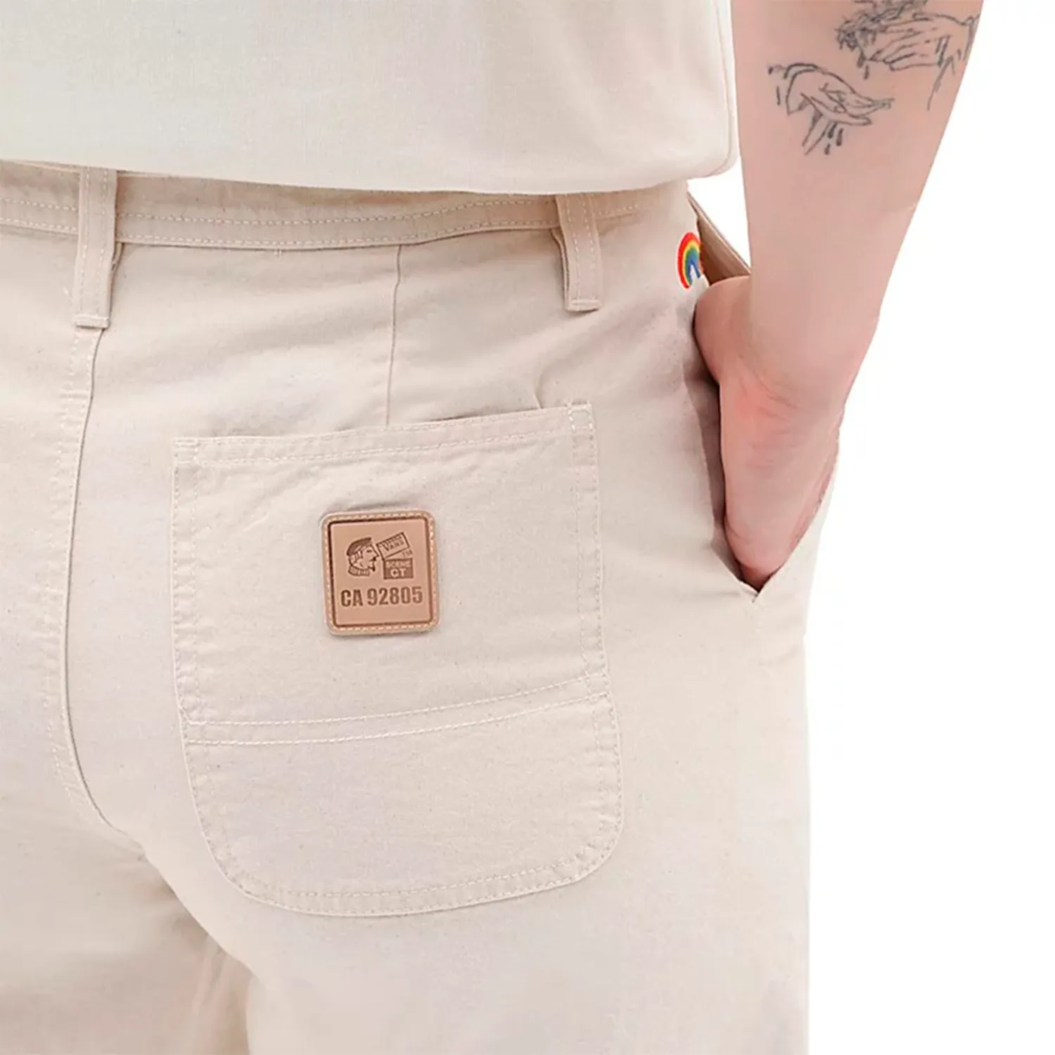 Calças bege claras com bolso traseiro e etiqueta castanha CA 92805, detalhe colorido arco-íris.