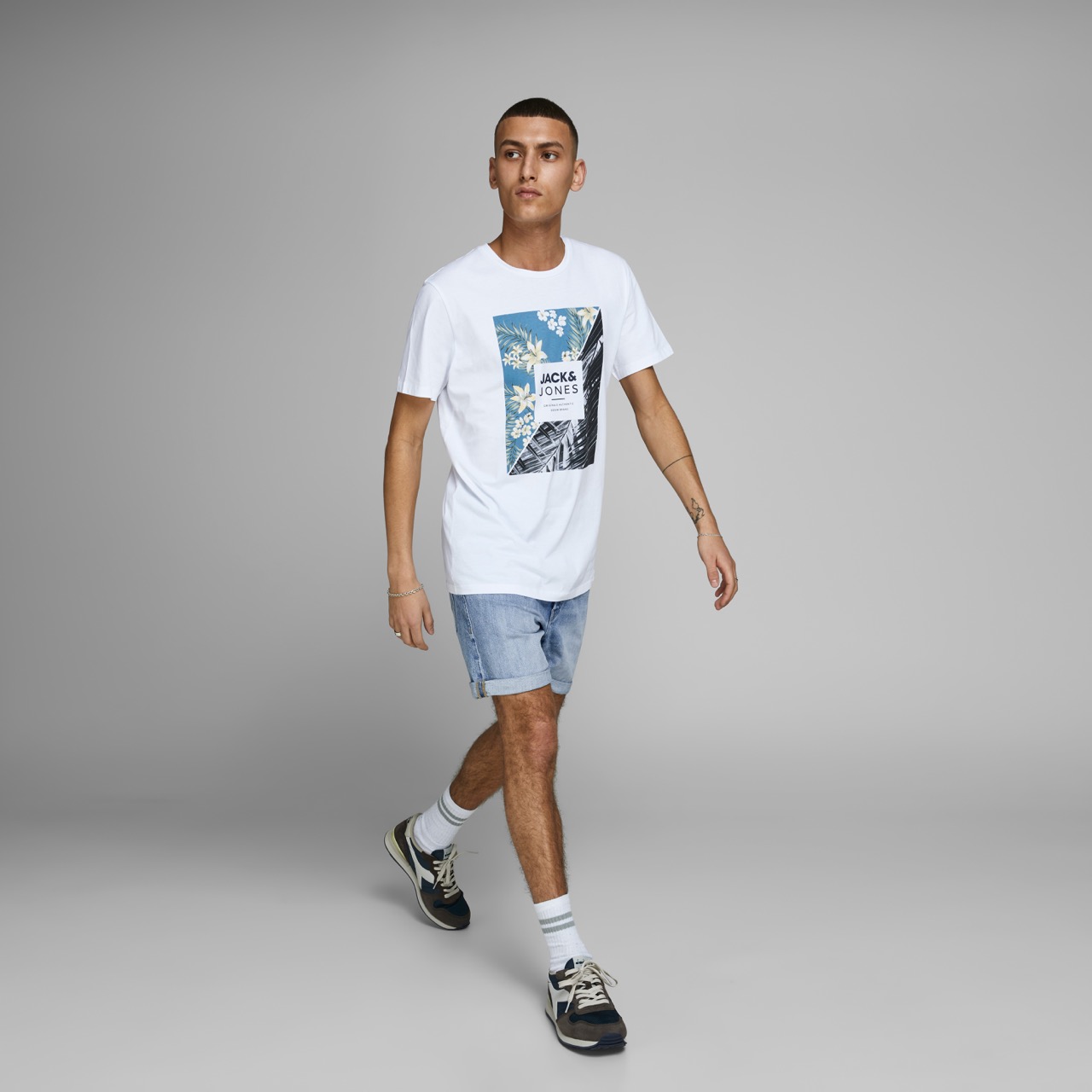 Homem com t-shirt branca estampada, calções de ganga e ténis