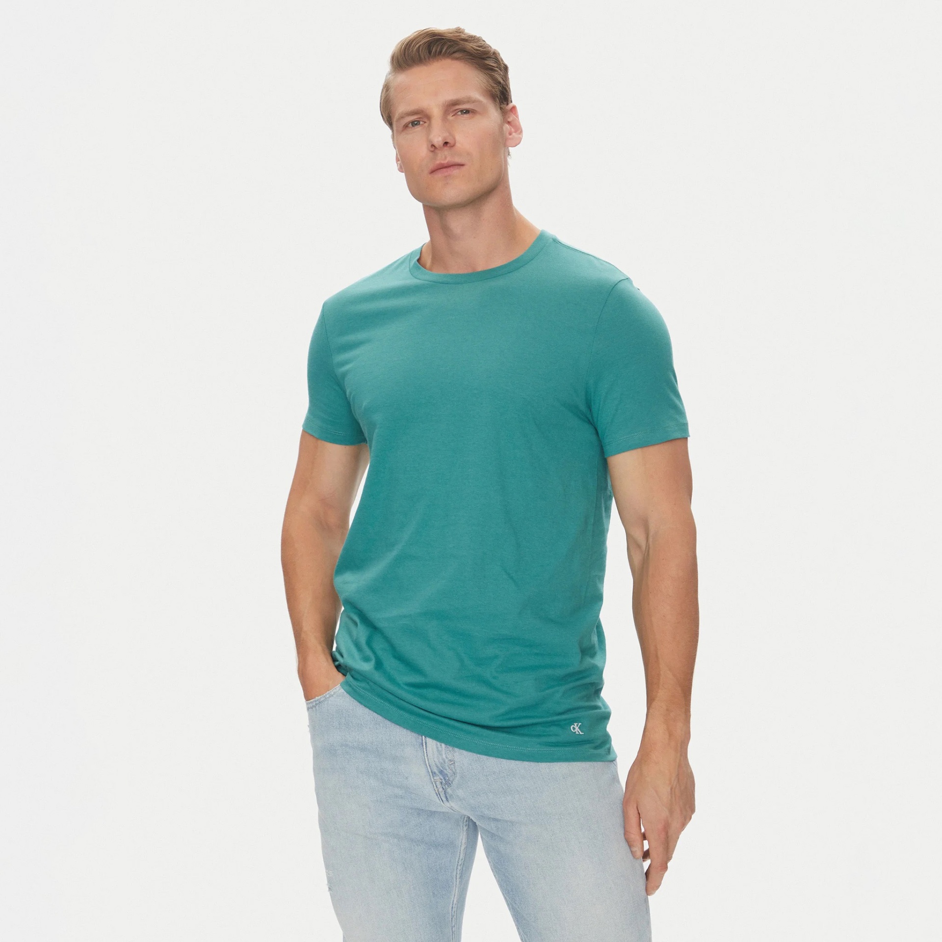 Homem com t-shirt verde-azulada e jeans claros em fundo branco