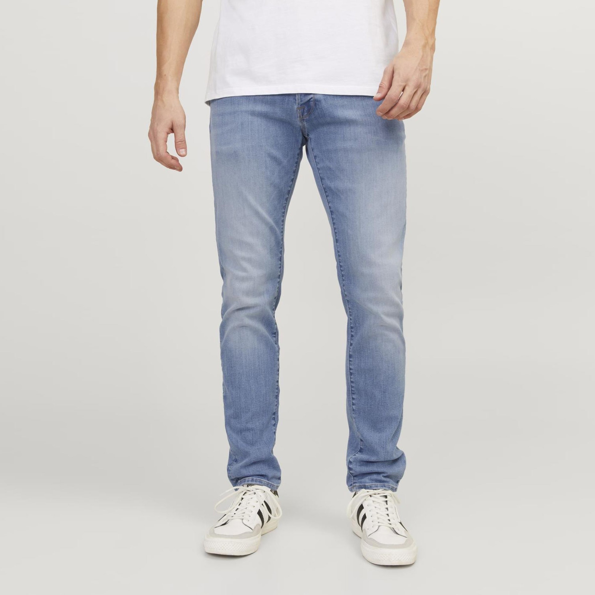 Calças de ganga azuis desbotadas usadas com t-shirt branca e sapatilhas brancas e pretas