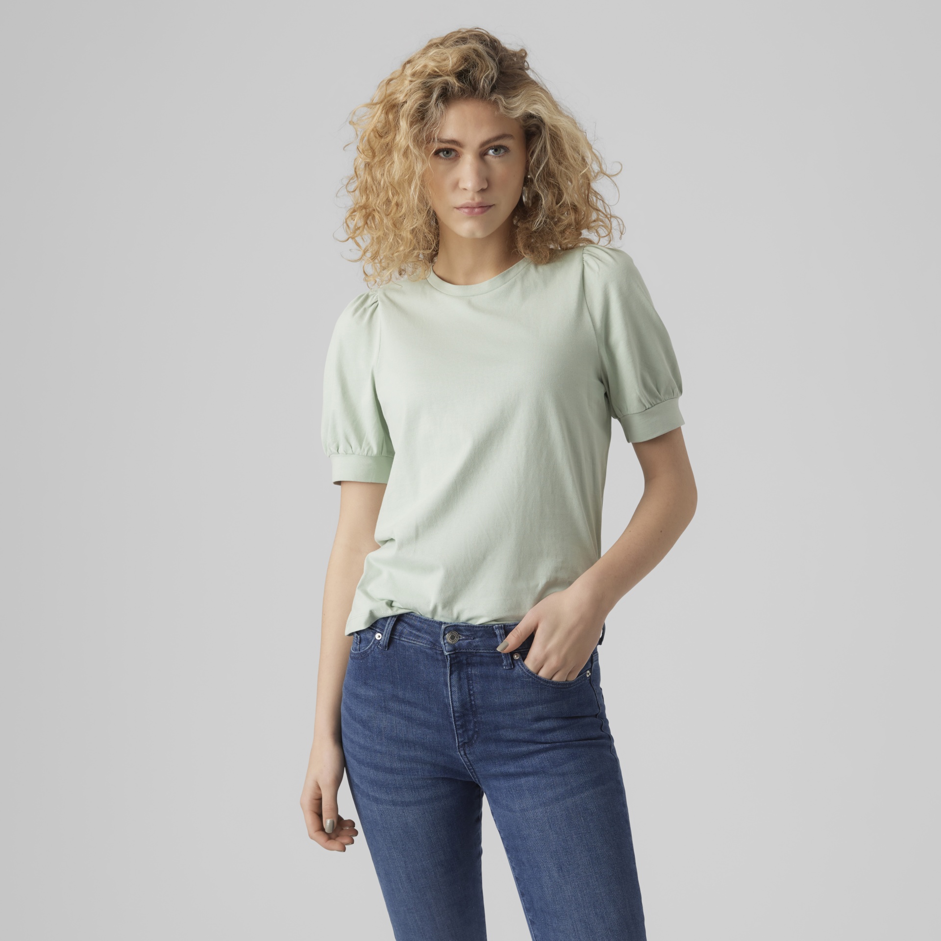 Mulher com t-shirt verde claro de mangas bufantes e calças de ganga azul