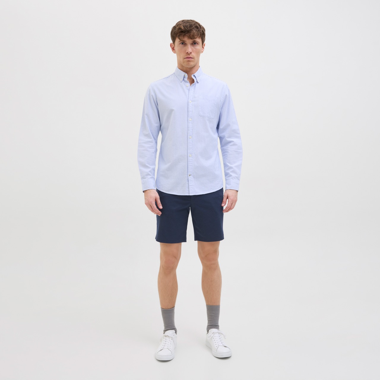 Homem com camisa azul clara listrada, calções azuis, meias cinzentas e sapatilhas brancas