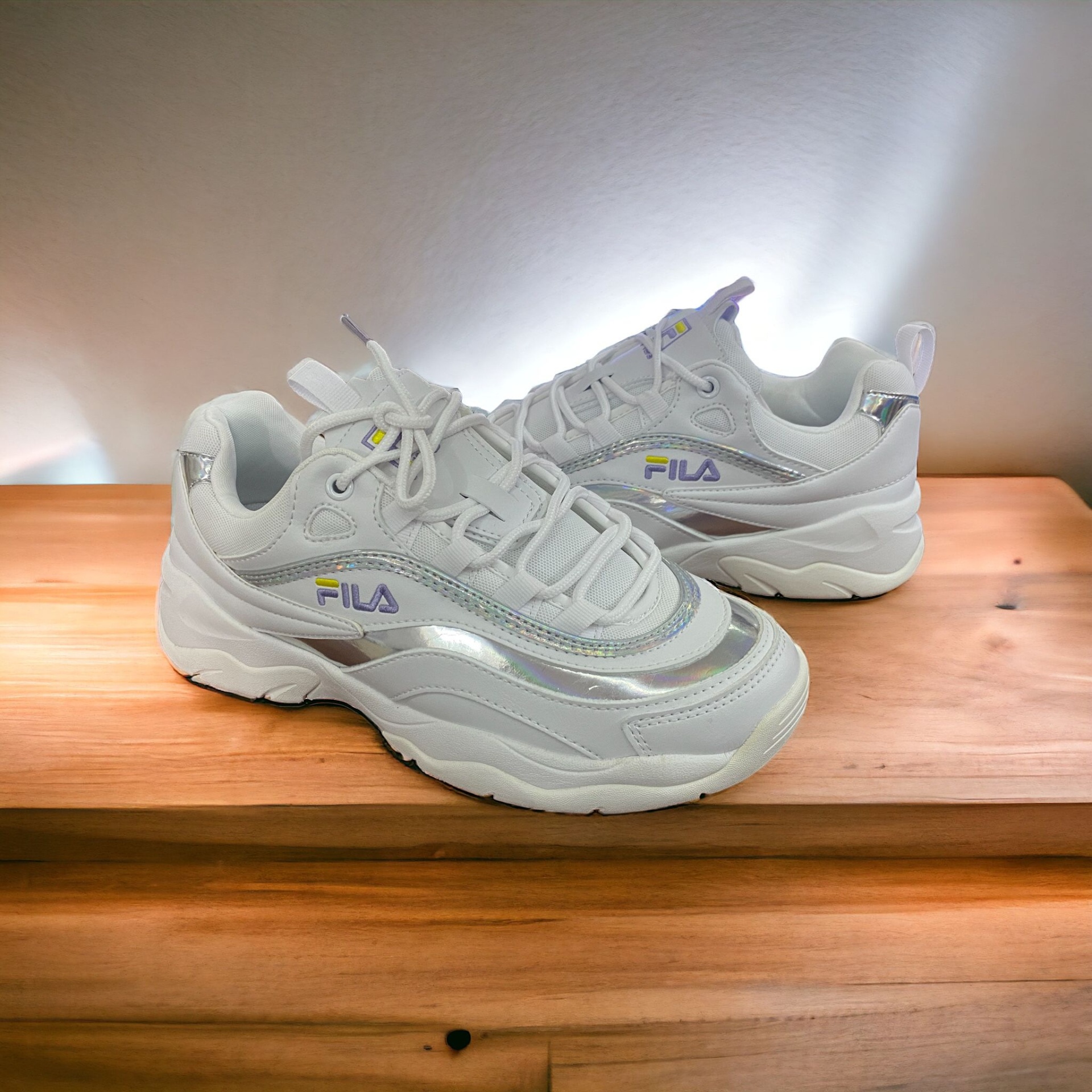 Sapatilhas brancas FILA com detalhes prateados sobre madeira clara