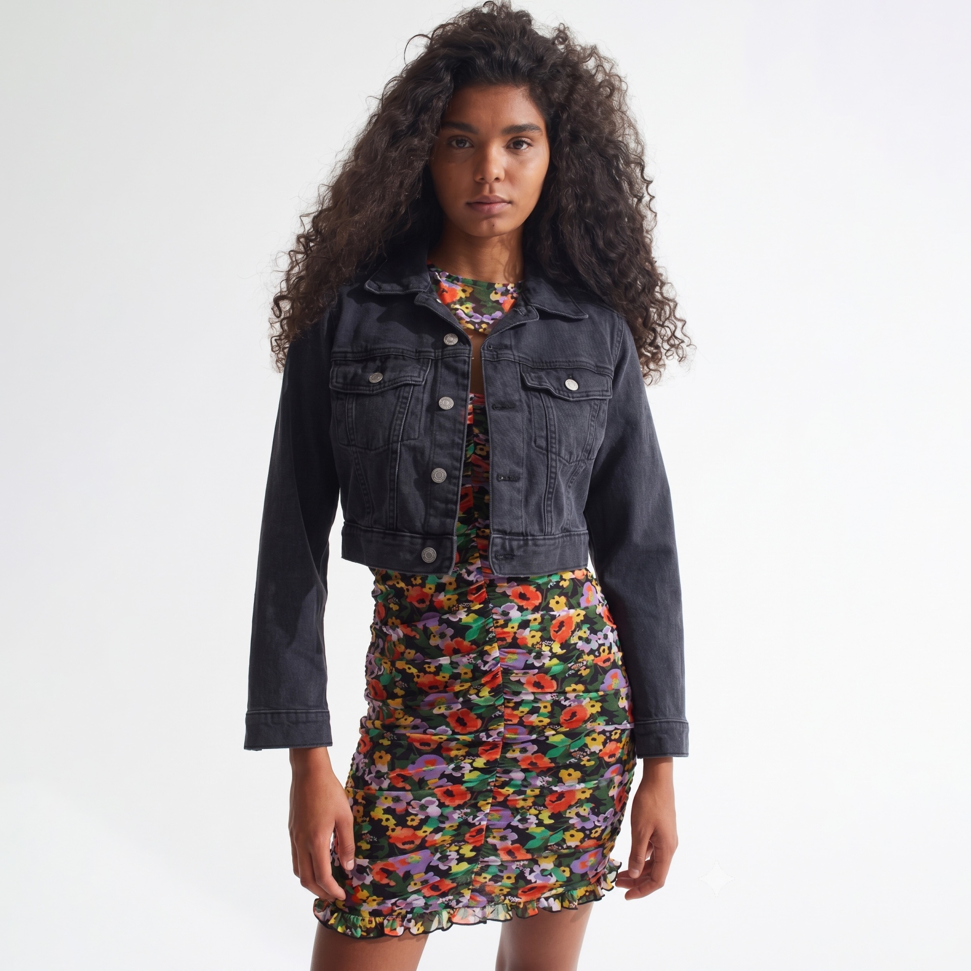 Mulher com blusão de ganga preto e vestido floral colorido com fundo branco.