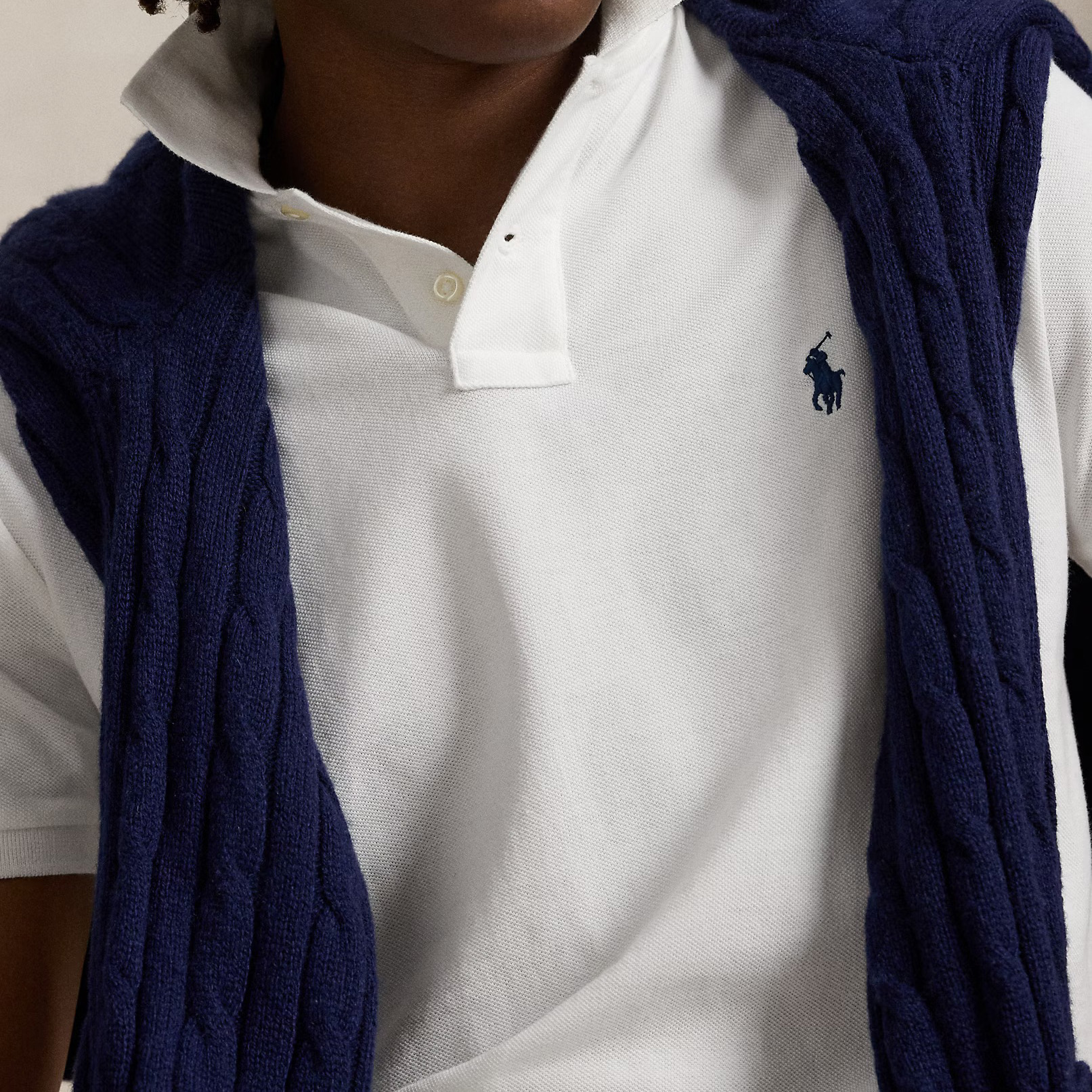 Pessoa com polo branco Polo Ralph Lauren e camisola azul de malha pendurada nos ombros