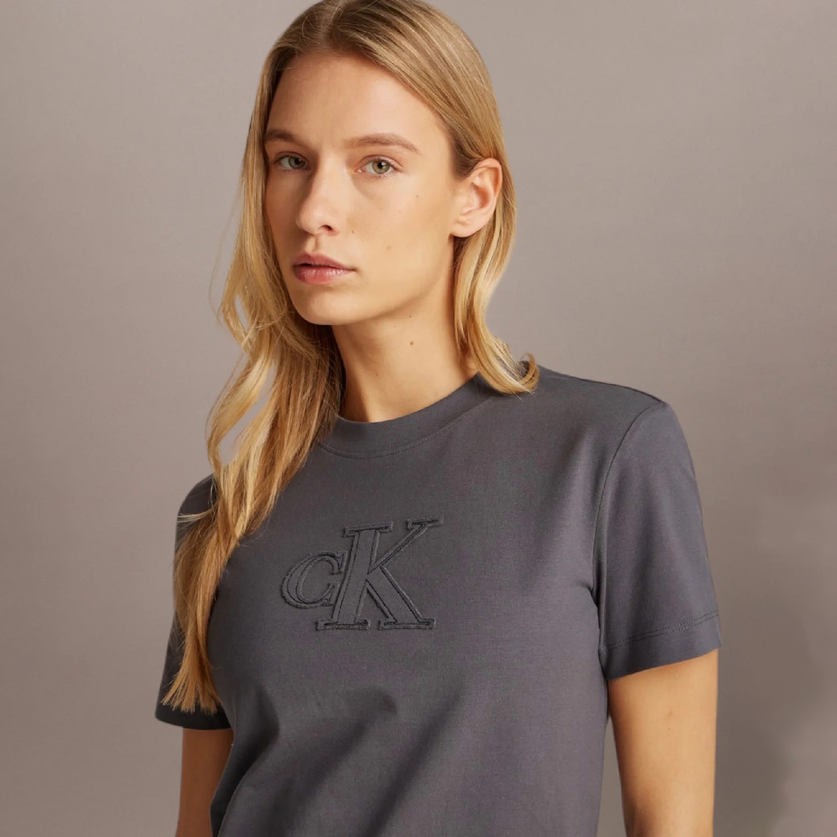 Mulher a usar t-shirt cinzenta escura com logótipo cK bordado no peito.