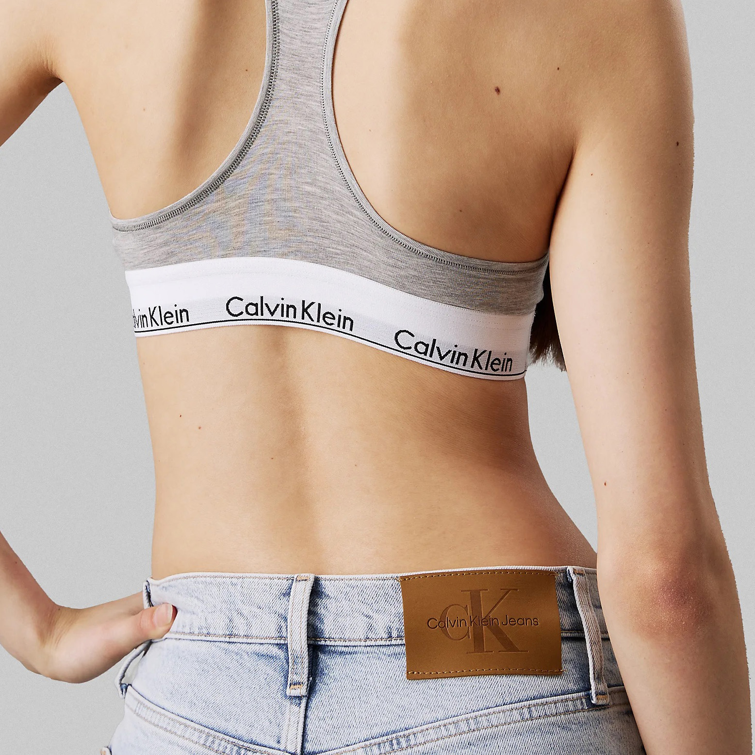 Top desportivo cinzento com logo Calvin Klein e calças jeans azuis com etiqueta Calvin Klein Jeans