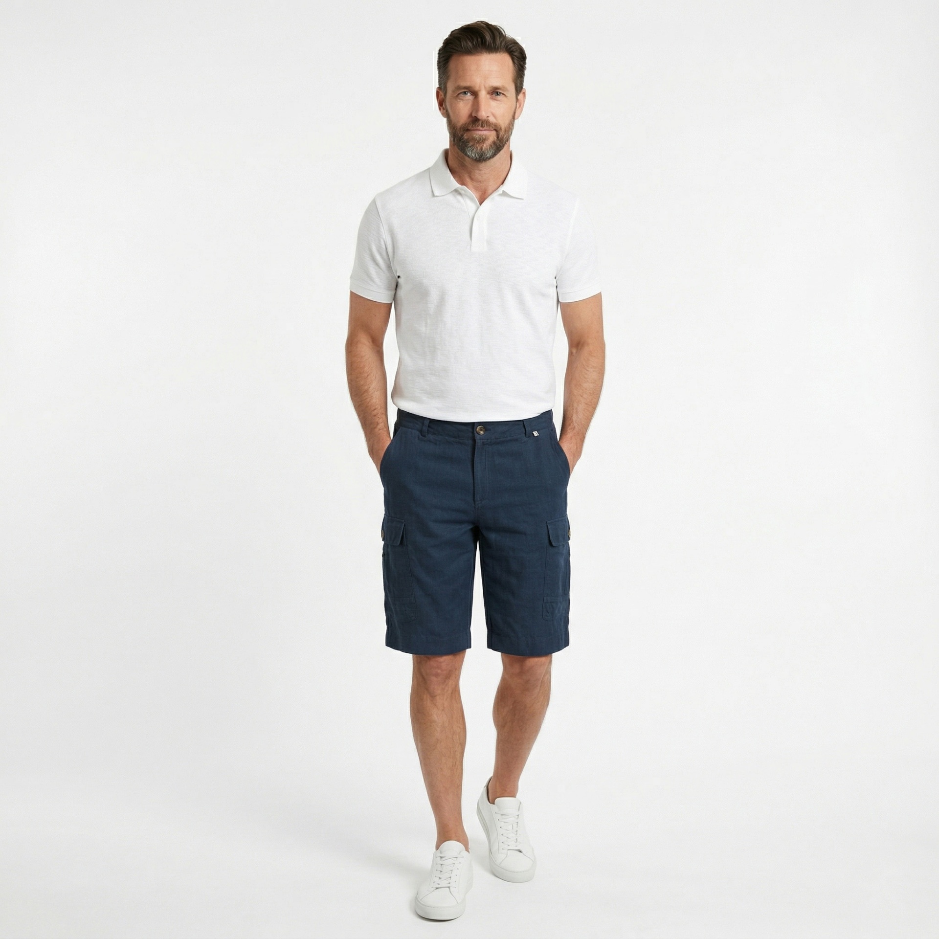 Homem com camisola polo branca e calções azuis escuros numa pose frontal sobre fundo branco.