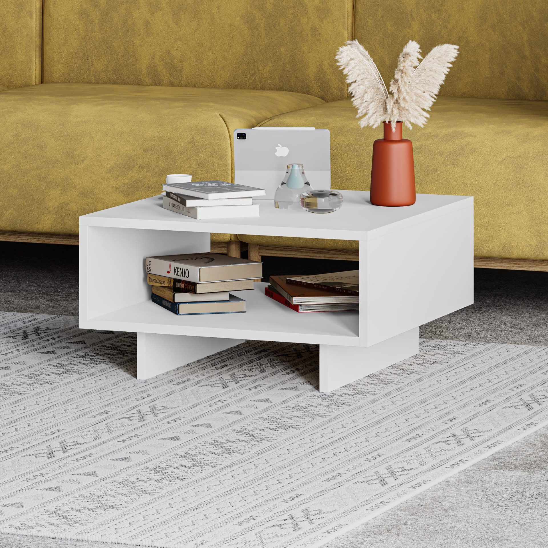 Mesa de centro branca com estantes, livros, vaso terracota com penas, jarra de vidro e tablet em sala com sofá amarelo