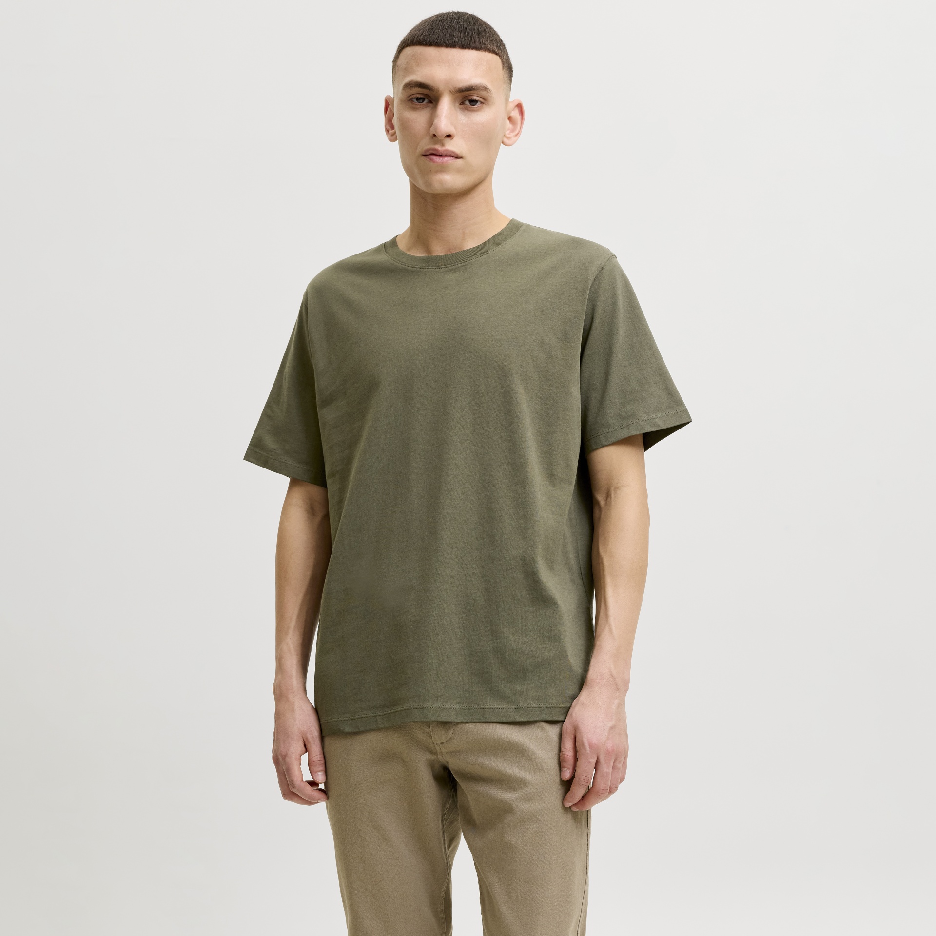 Homem com t-shirt verde-oliva e calças beges em fundo branco