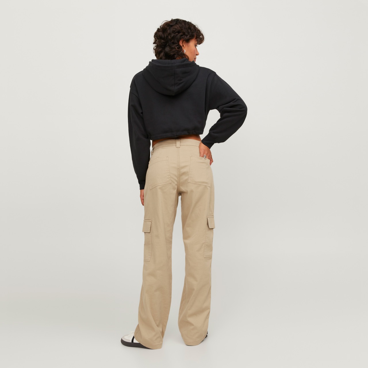 Modelo de costas usando calças cargo bege e hoodie preto com capuz em fundo branco