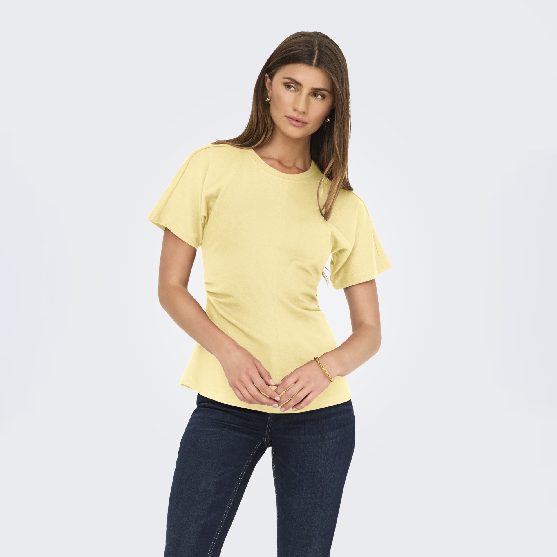 T-shirt feminina amarelo claro e calças de ganga azul escuro num fundo branco