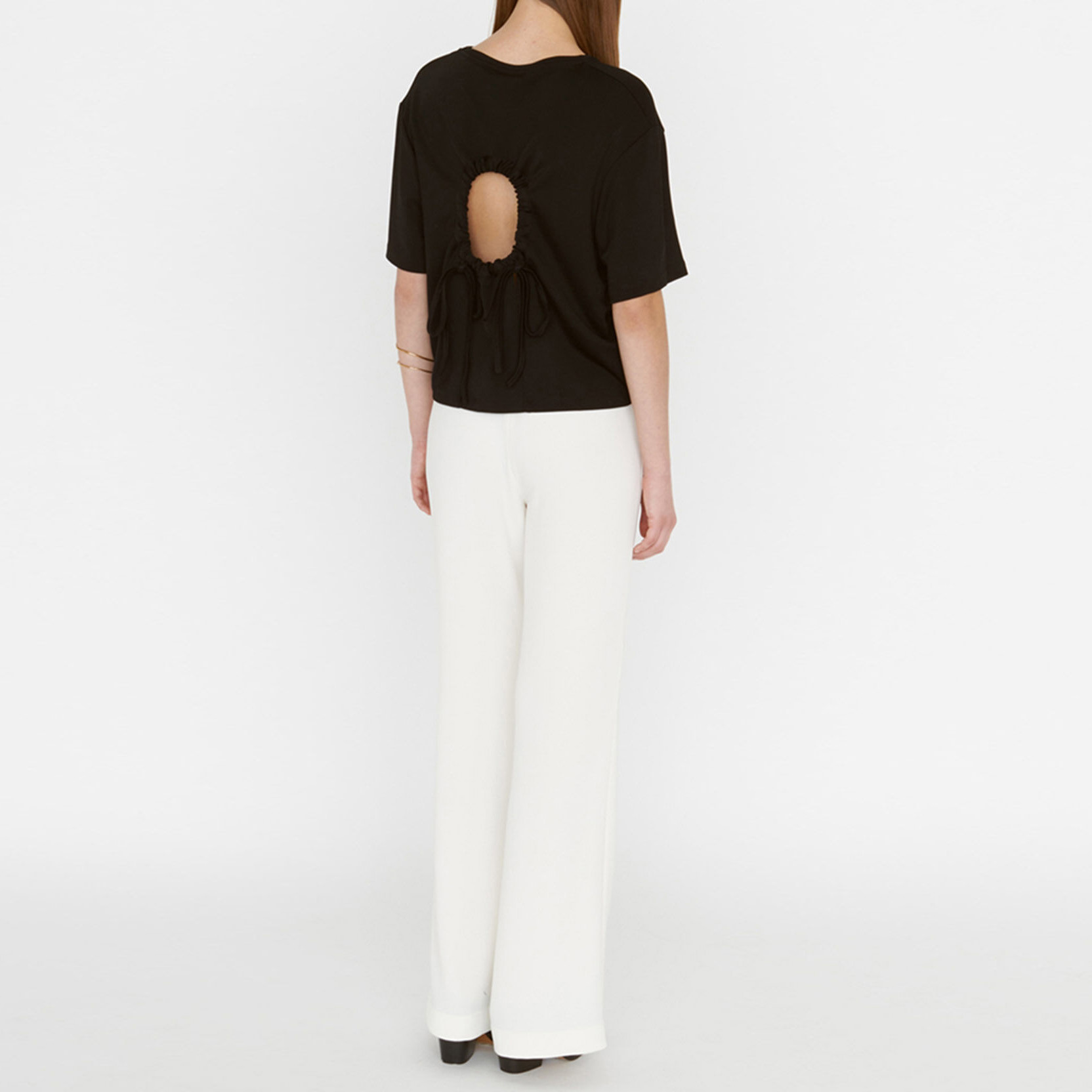 T-shirt preta com abertura nas costas e calças brancas em modelo de costas