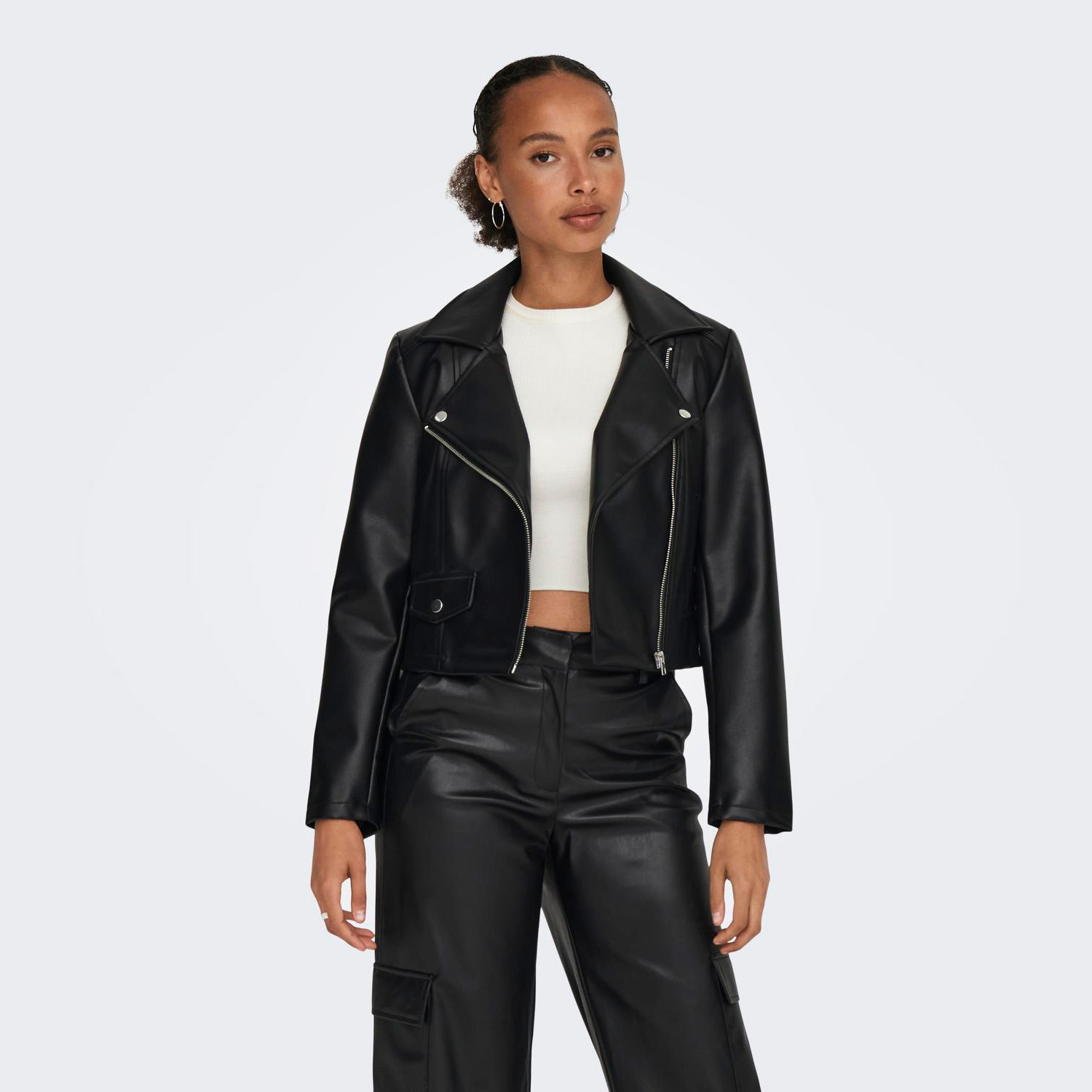 Mulher a usar casaco preto estilo biker em tecido sintético e calças pretas largas com camisa branca de manga curta