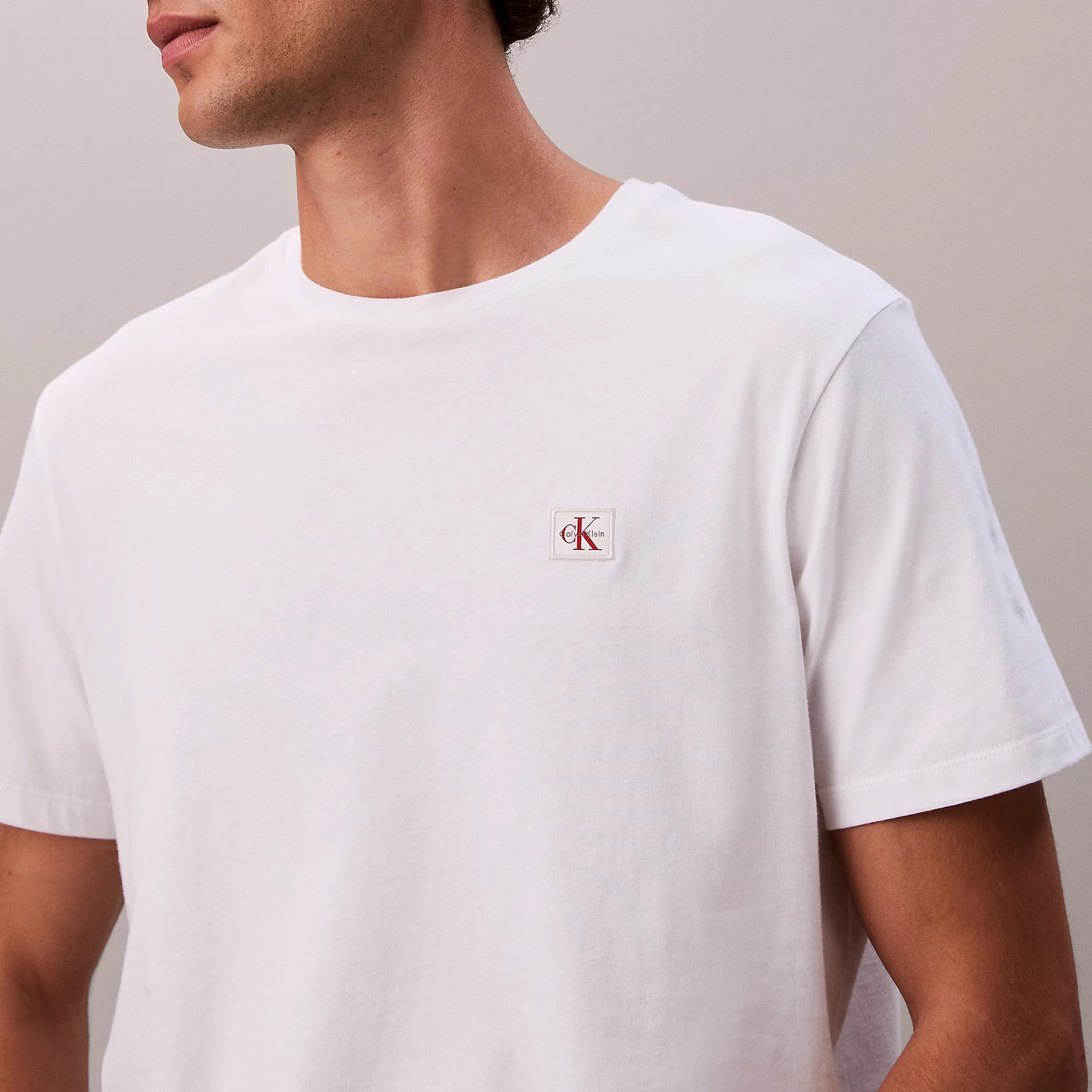 T-shirt branca com logo Calvin Klein no peito e fundo cinza claro