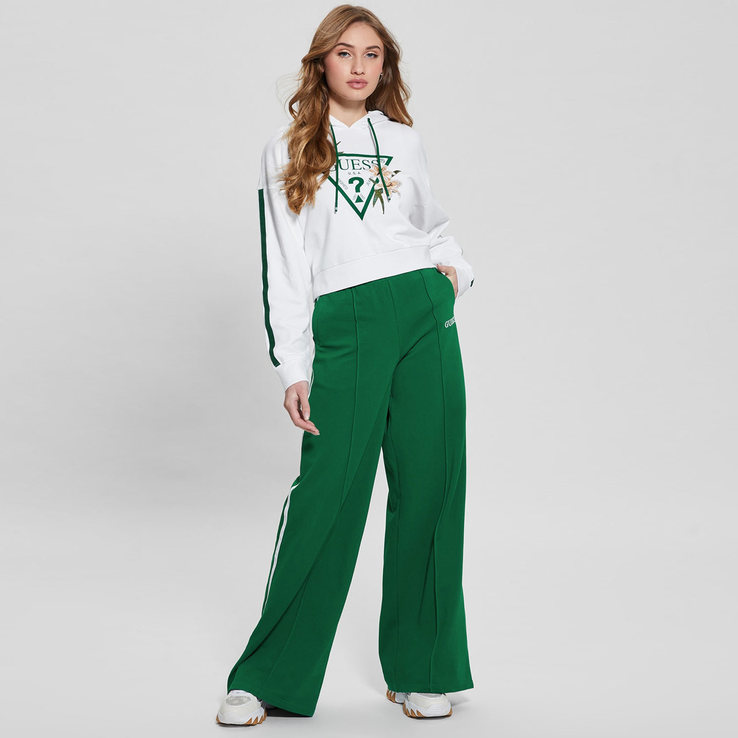 Mulher com conjunto branco e verde GUESS com sweatshirt e calças largas.