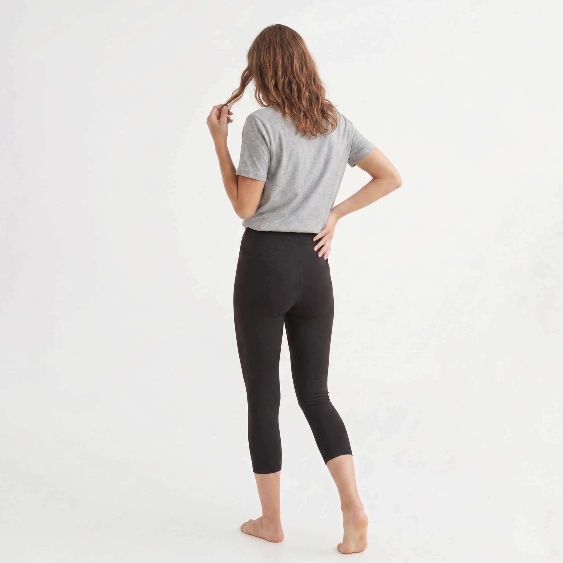 Mulher de costas com t-shirt cinza e leggings pretas em fundo branco