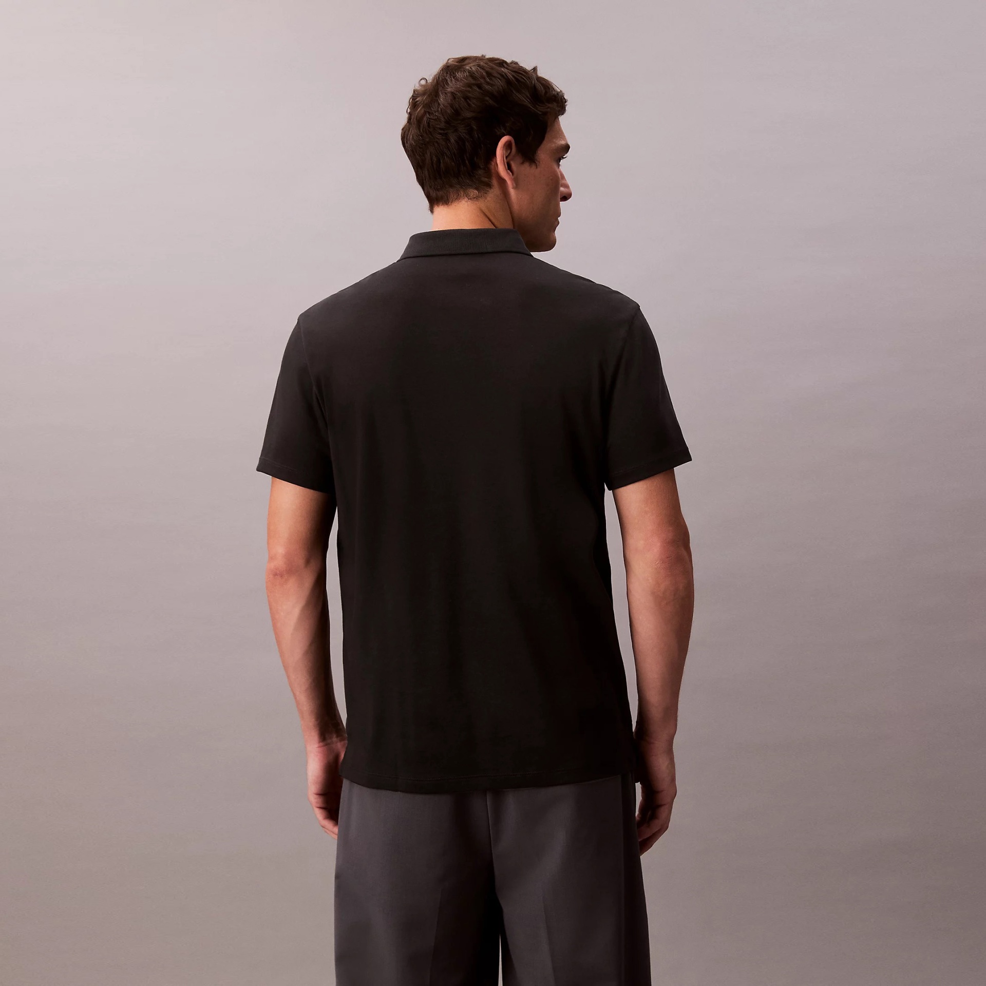 Homem de costas a usar polo preto de manga curta e calças cinza