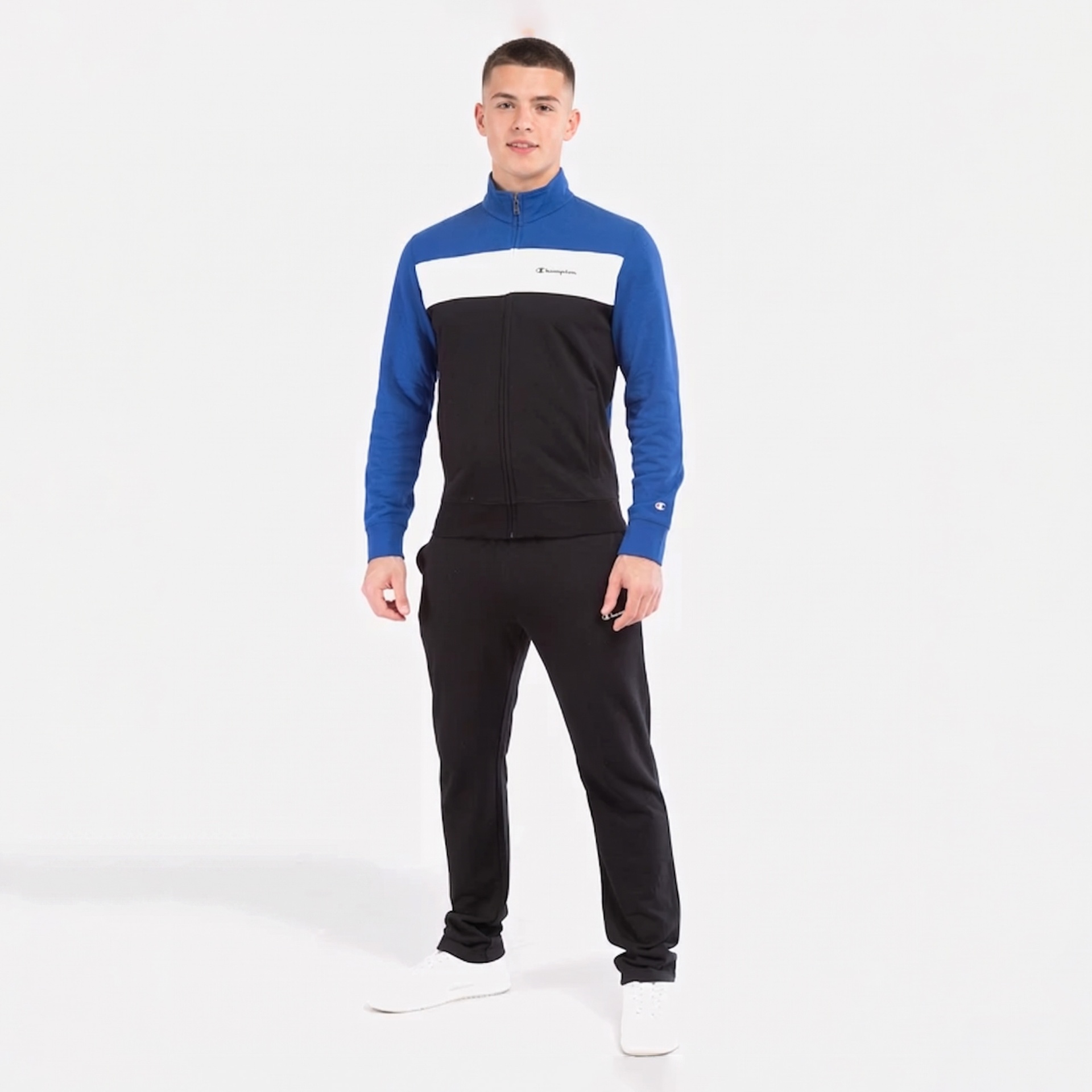 Conjunto desportivo azul, branco e preto com texto Champion e calças pretas num fundo branco.