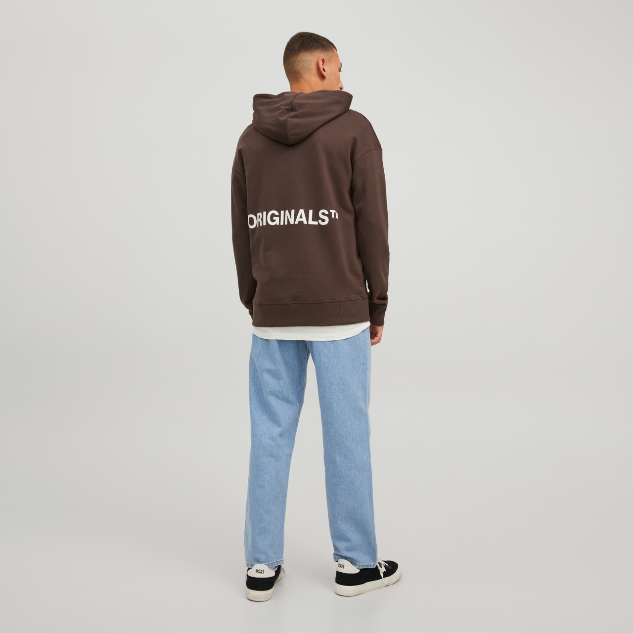 Sweatshirt castanha com capuz e texto ORIGINALS™ nas costas, usada com calças de ganga e sapatos pretos